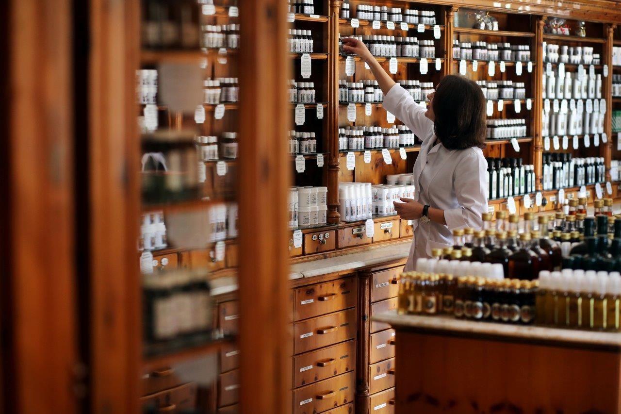 Eine Apothekerin in einem traditionellen Apothekenladen, umgeben von Holzregalen voller Flaschen und Gläser.