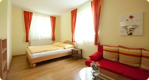 Helles Zimmer mit Doppelbett, rotem Sofa und Vorhängen.