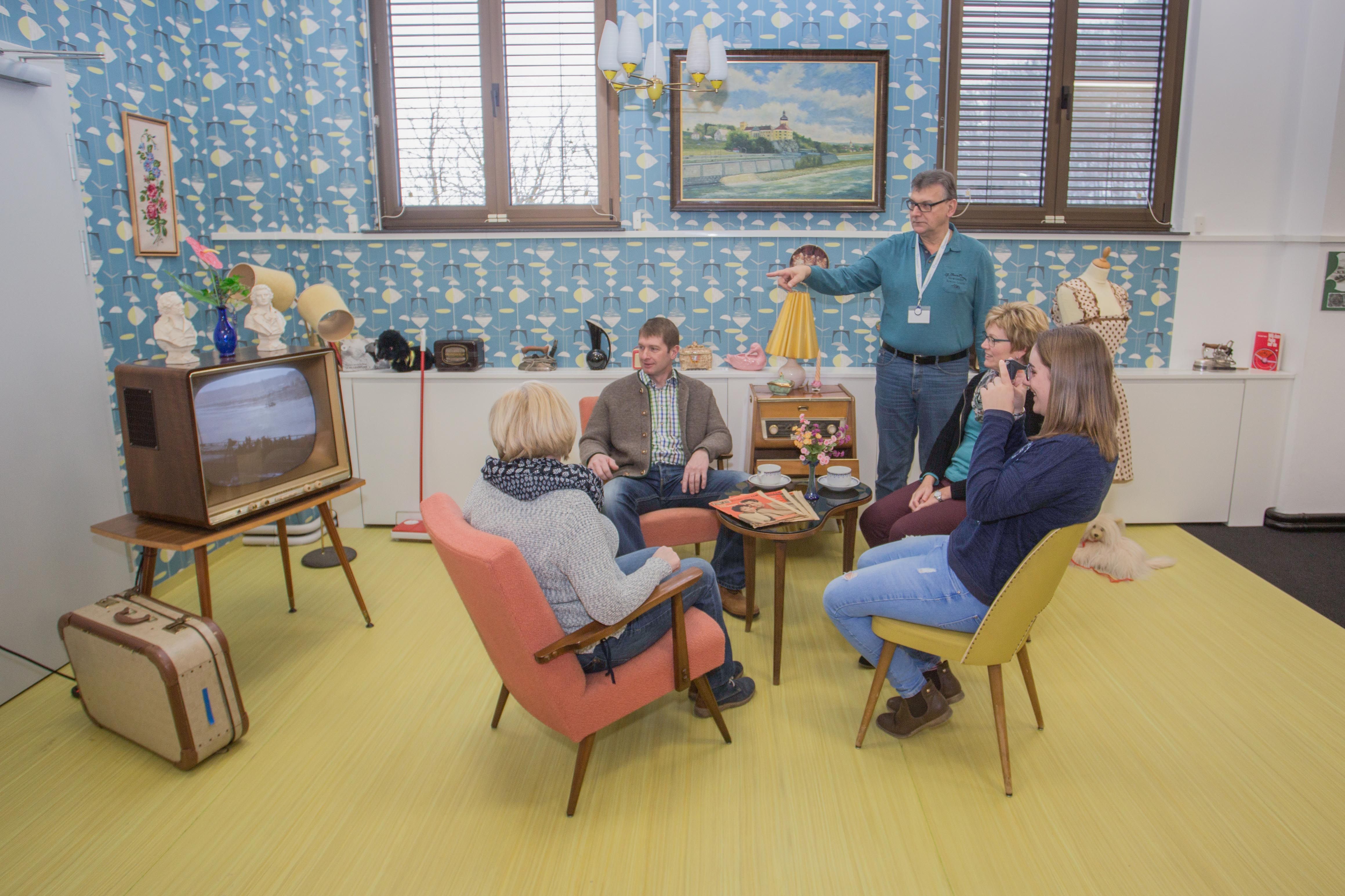 Gruppe von Menschen in einem Wohnzimmer im Stil der 60er Jahre mit Retro-Möbeln und Dekoration.