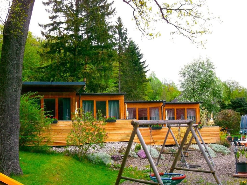 Ein Landgasthof mit Holzfassade und Spielplatz im Vordergrund, umgeben von Bäumen.