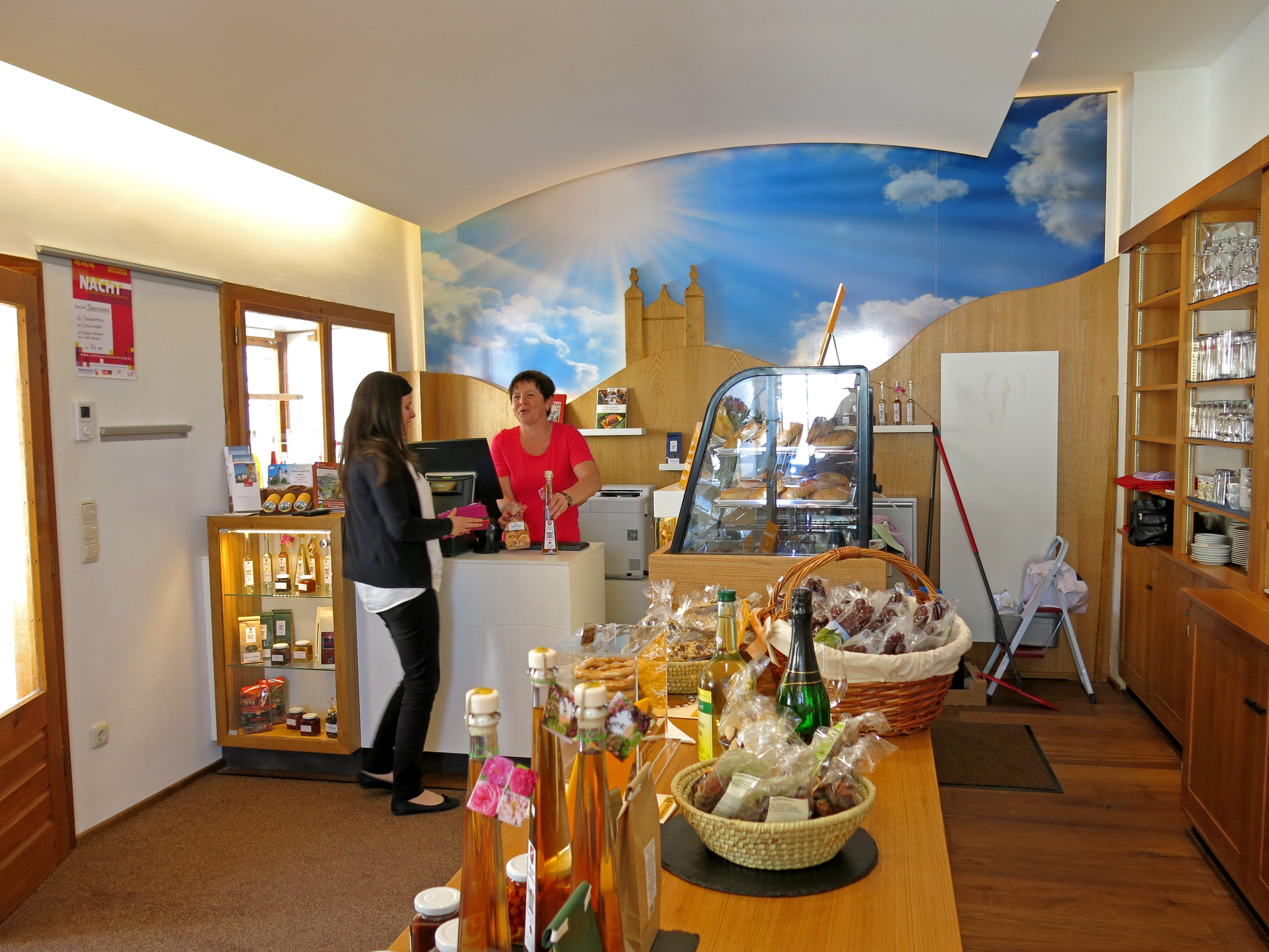 Innenansicht eines Besucherzentrums mit zwei Frauen an der Theke und verschiedenen Produkten auf einem Tisch.