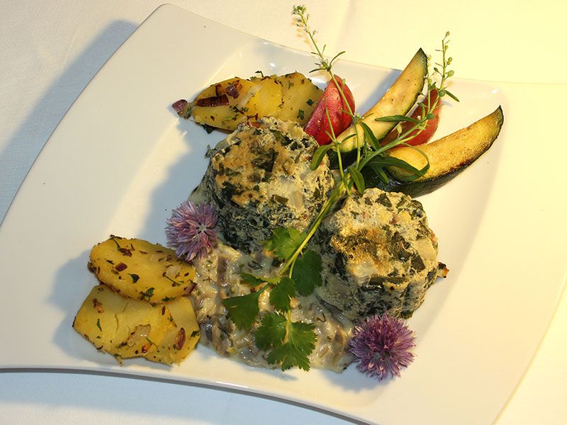 Ein Teller mit Spinatknödeln, Kartoffeln und Gemüse dekorativ angerichtet.