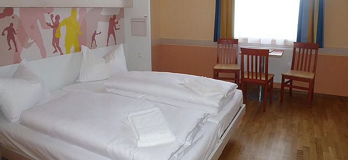 Hotelzimmer mit Doppelbett, zwei Stühlen und einem Tisch vor einem Fenster.