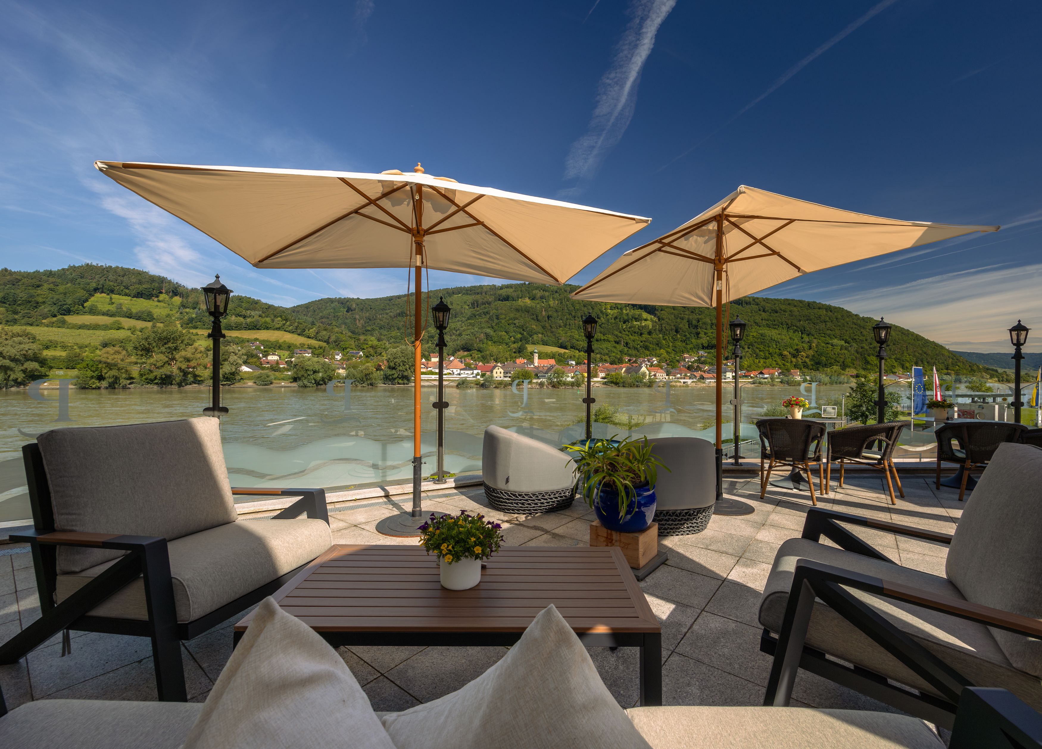 Terrasse mit Blick auf die Donau und umliegende Hügel, ausgestattet mit Sonnenschirmen und Sitzmöbeln.
