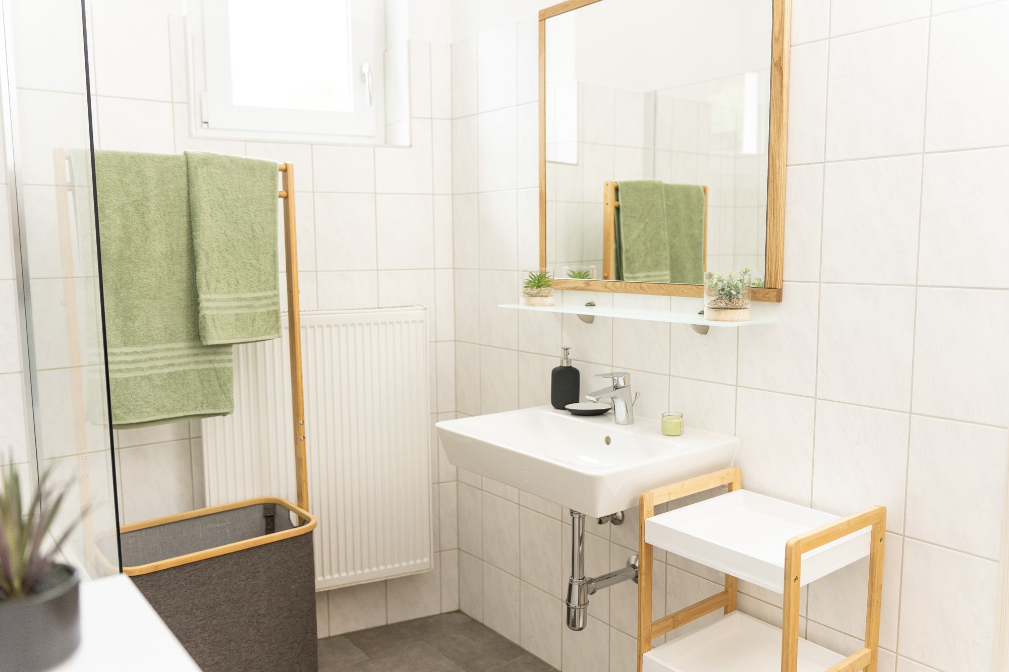 Helles Badezimmer der Ferienwohnung Turmblick mit Waschbecken, Spiegel, grünen Handtüchern und Duschbereich.