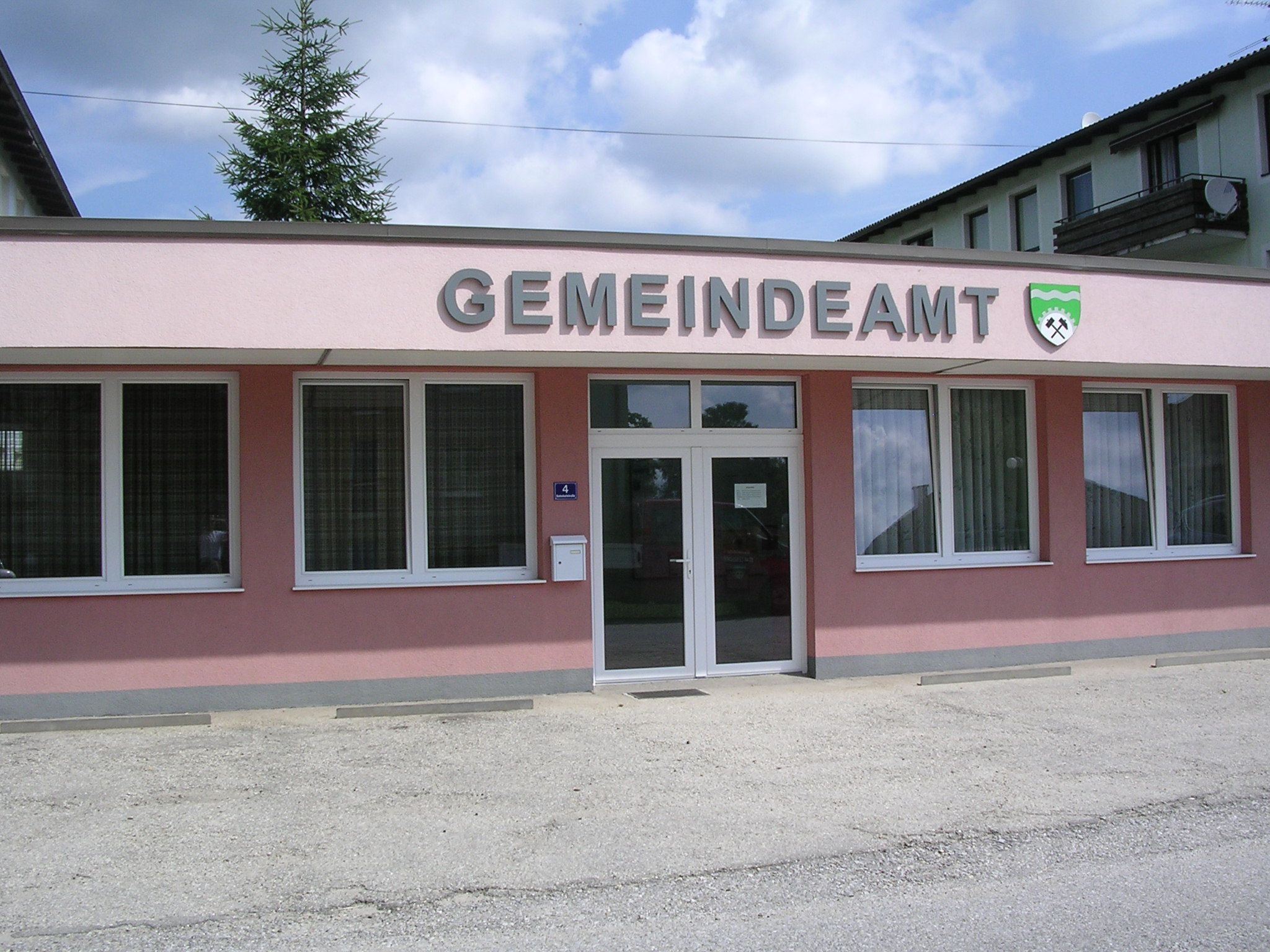Außenansicht eines rosa Gebäudes mit der Aufschrift 'GEMEINDEAMT' und einem Wappen.