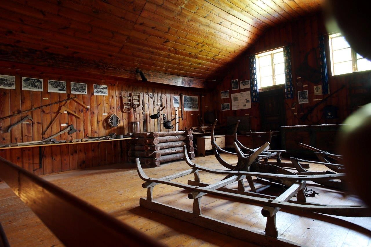 Innenansicht eines Museums mit Holzwänden, alten Werkzeugen und Schlitten.