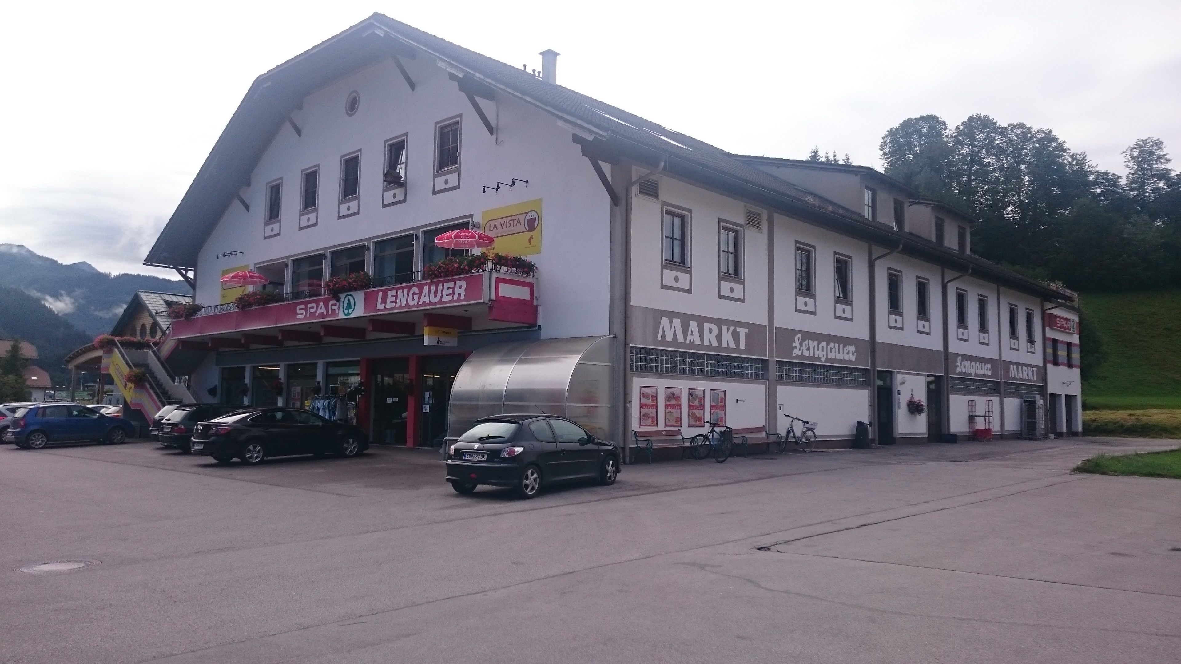 Gebäude mit Spar-Lengauer-Markt und Post-Partner-Schild, Autos und Fahrräder davor.