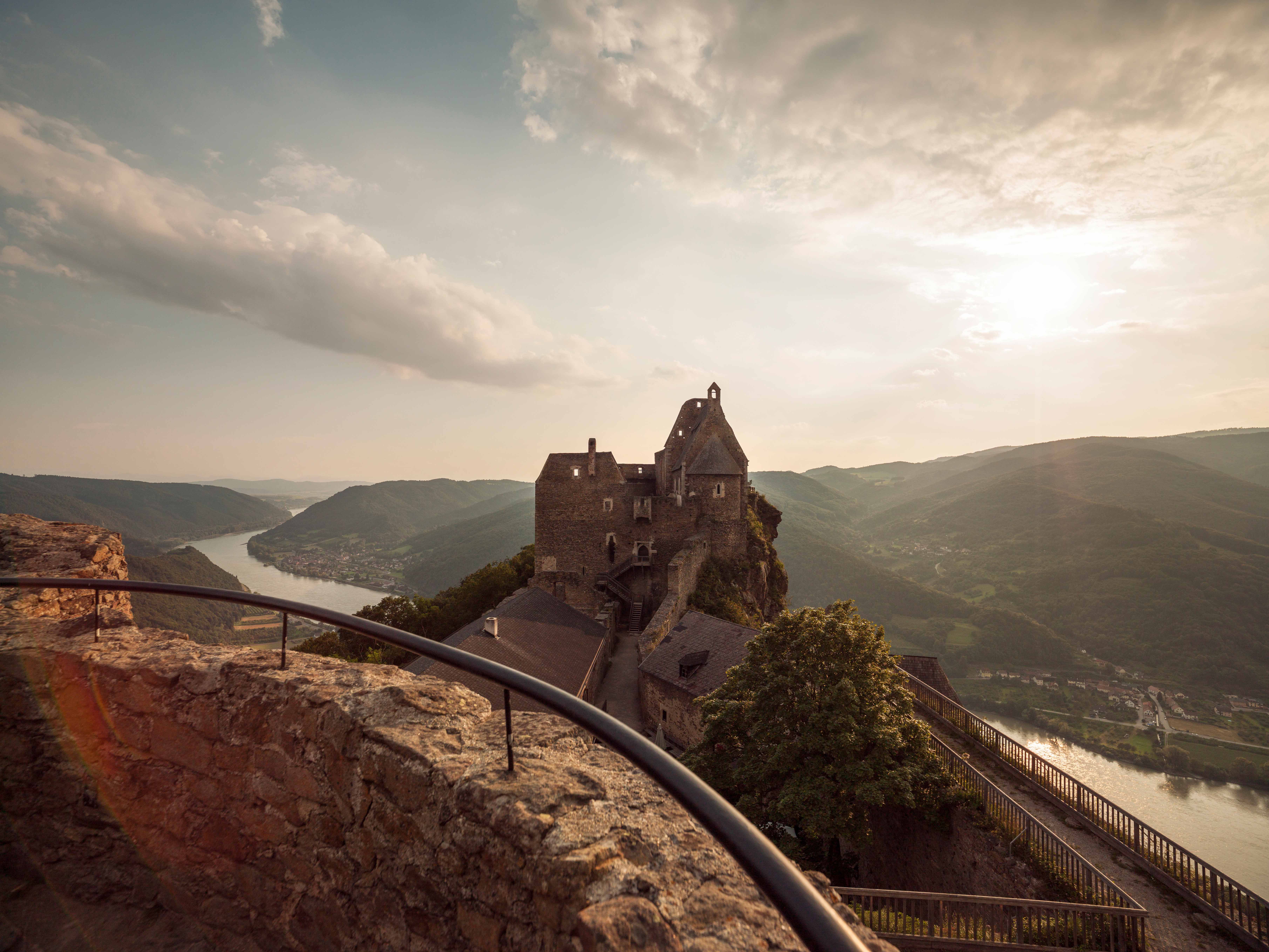 Burg Aggstein im Sommer mit Blick auf die Donau und umliegende Hügel.