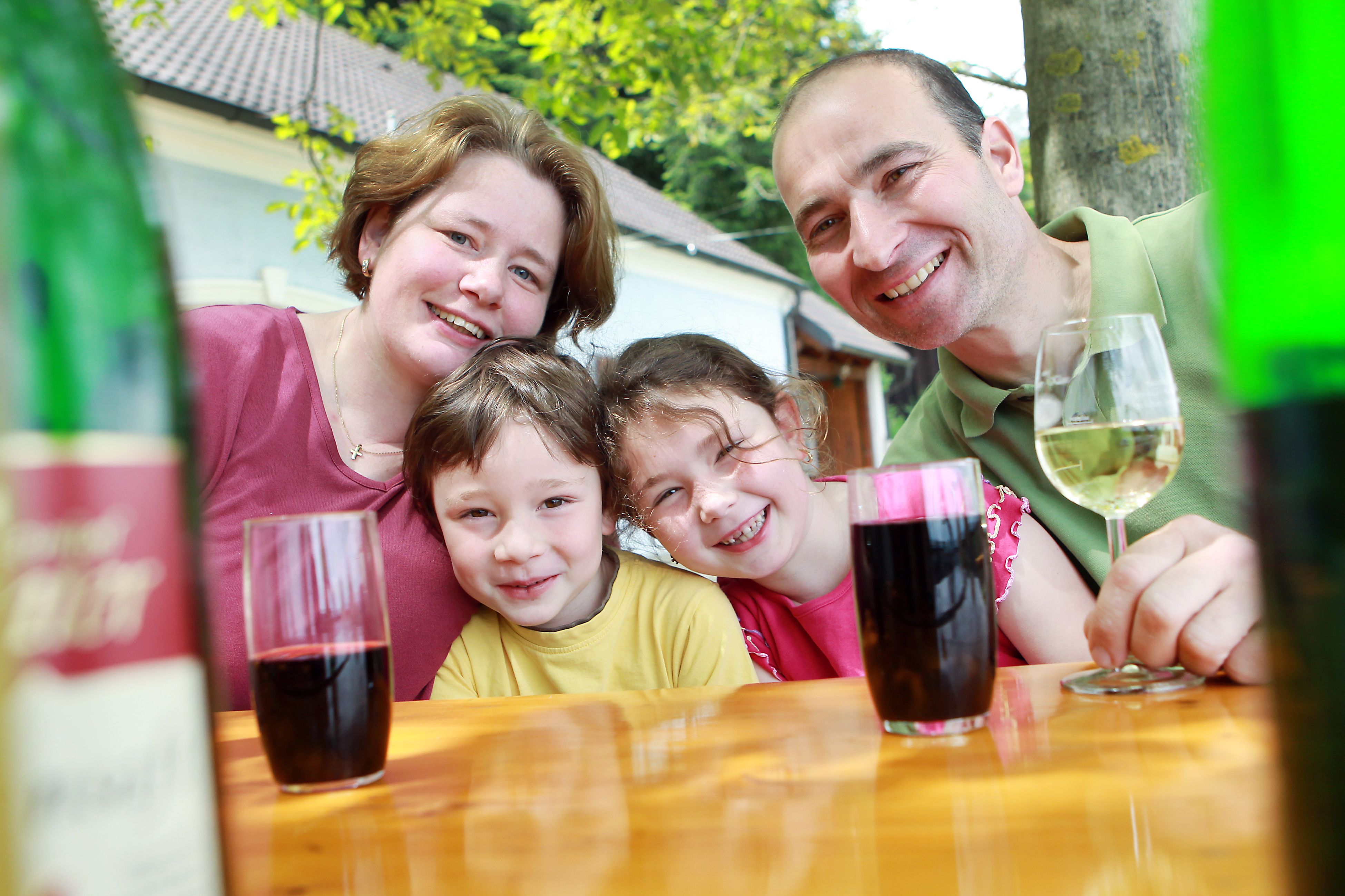 Familie sitzt an einem Tisch im Freien und lächelt in die Kamera.