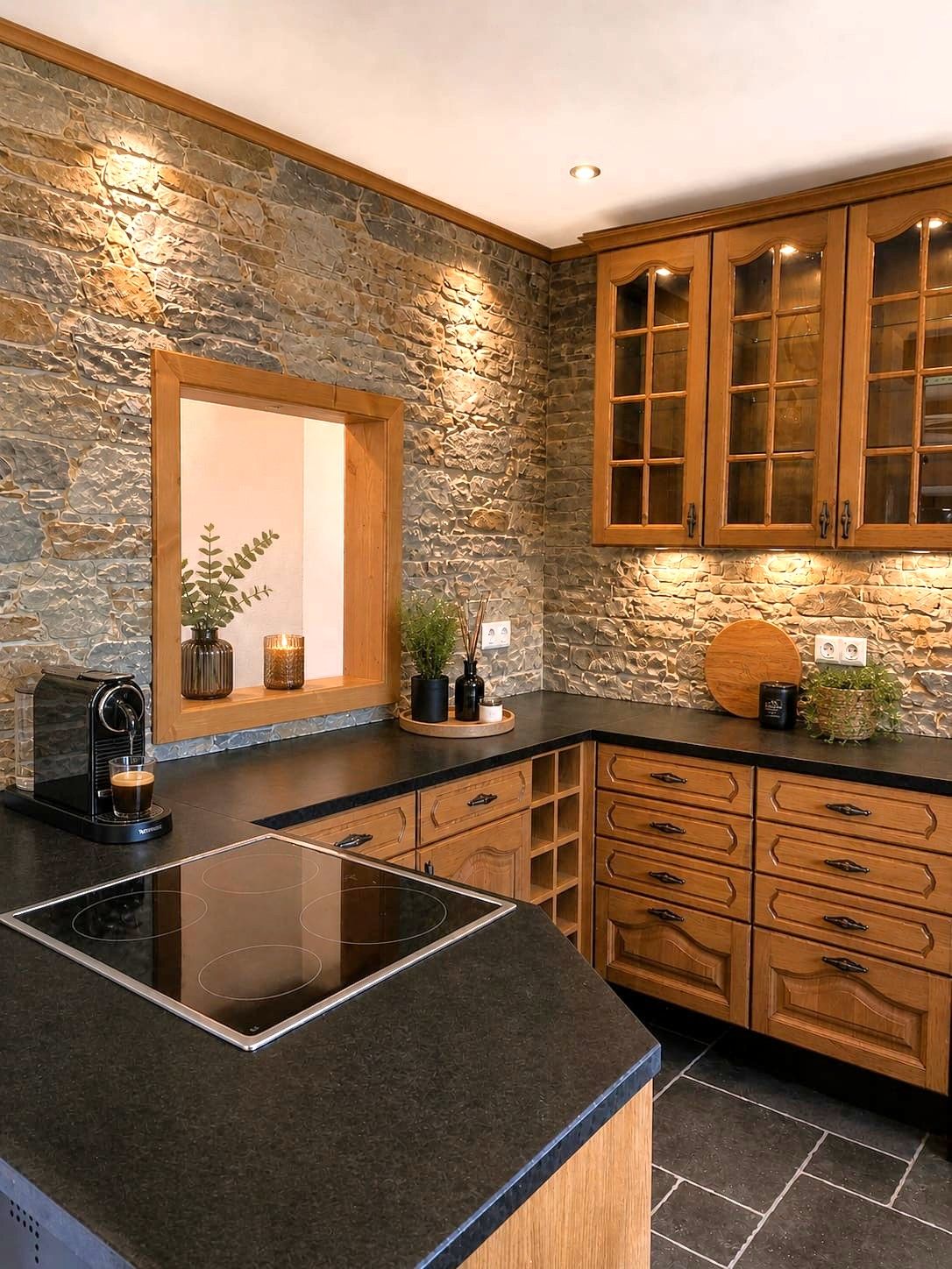 Küche mit Steinwand, Holzschränken und schwarzer Arbeitsplatte.