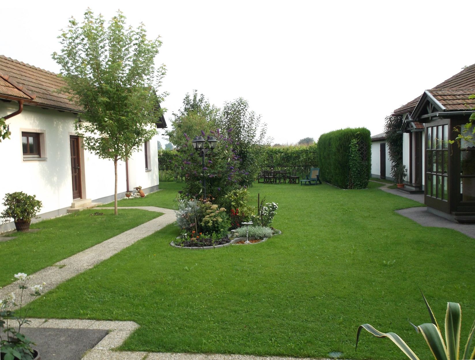 Sehr gepflegter Garten mit Blick auf Stauden und Bäume, im Hintergrund ein Teil des Gebäudes.