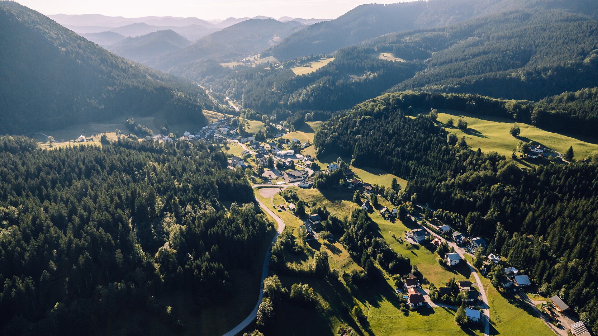 Luftaufnahme von Lackenhof am Ötscher mit dem Ort inmitten bewaldeter Berge und grüner Wiesen.