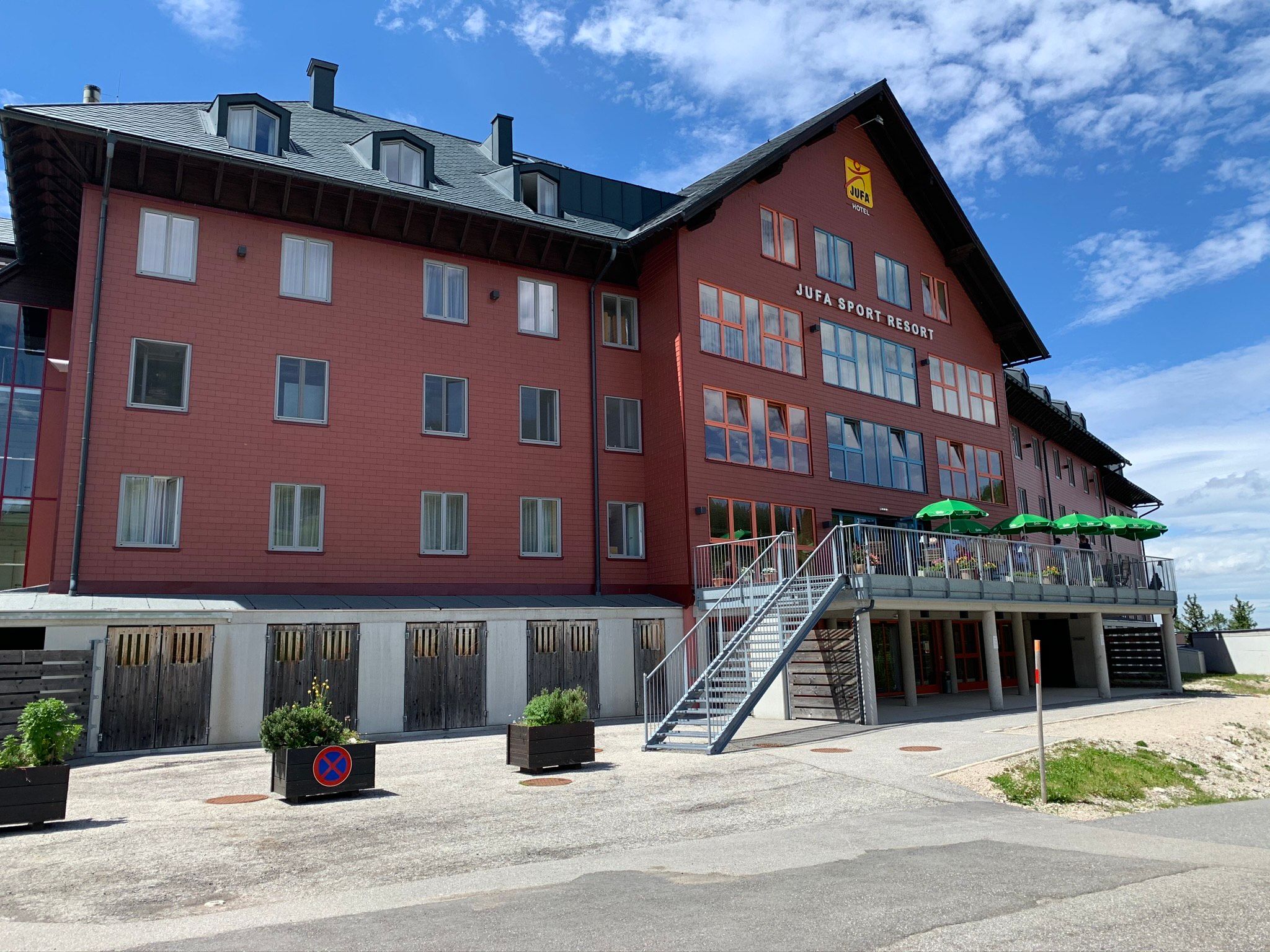 JUFA Sport Resort Hochkar mit roter Fassade und Terrasse mit grünen Sonnenschirmen.
