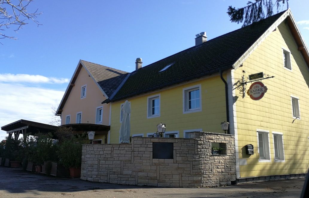 Gelbes Landgasthaus mit Kaiser Bier Schild und Sonnenschirm im Vordergrund.