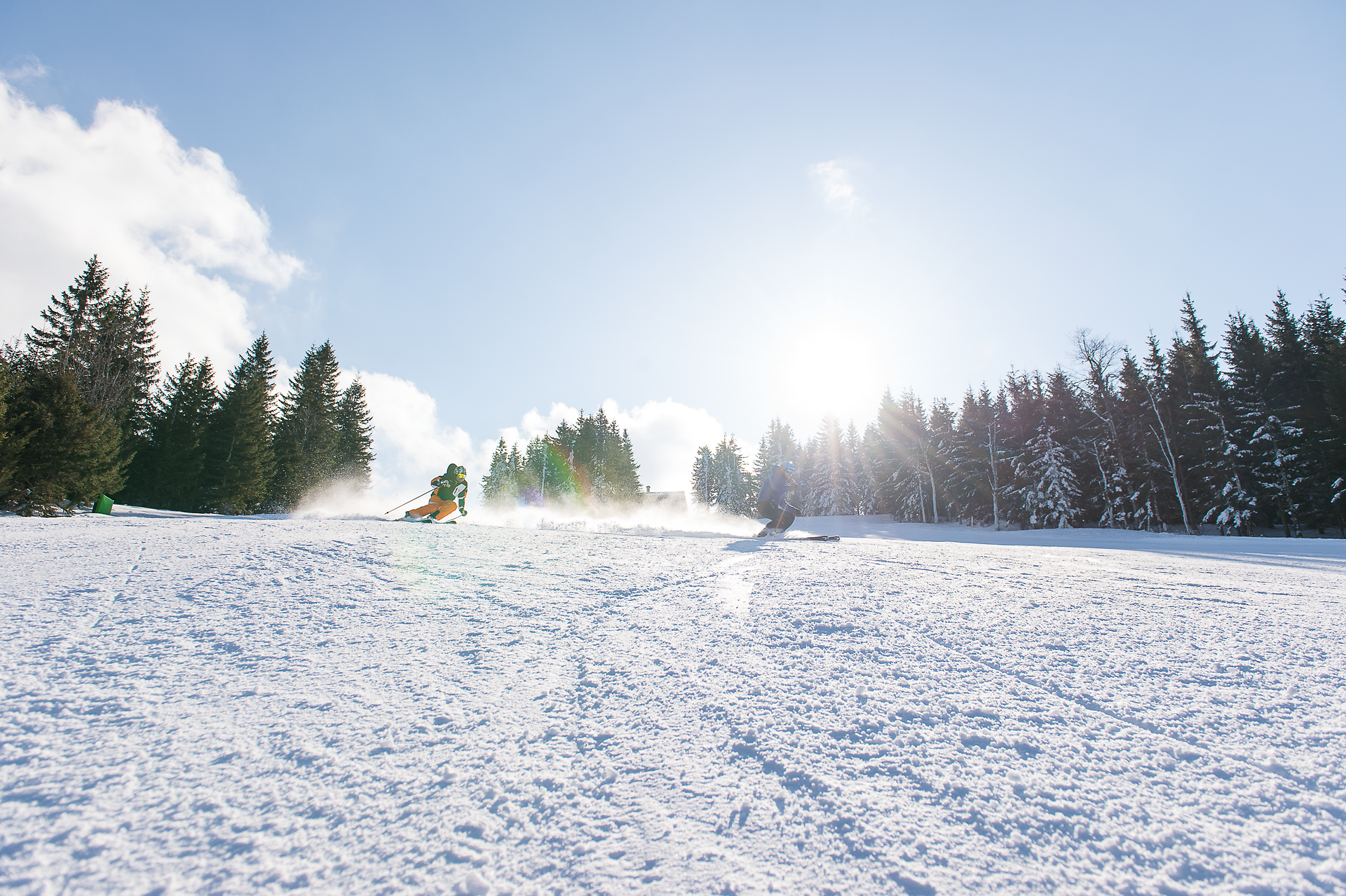 Die strahlende Sonne über den schneebedeckten Hängen schafft eine magische Atmosphäre, während Skifahrer elegant die Pisten hinuntergleiten. Die frische, klare Luft und die schneebedeckten Tannen laden zu einem unvergesslichen Winterabenteuer ein.