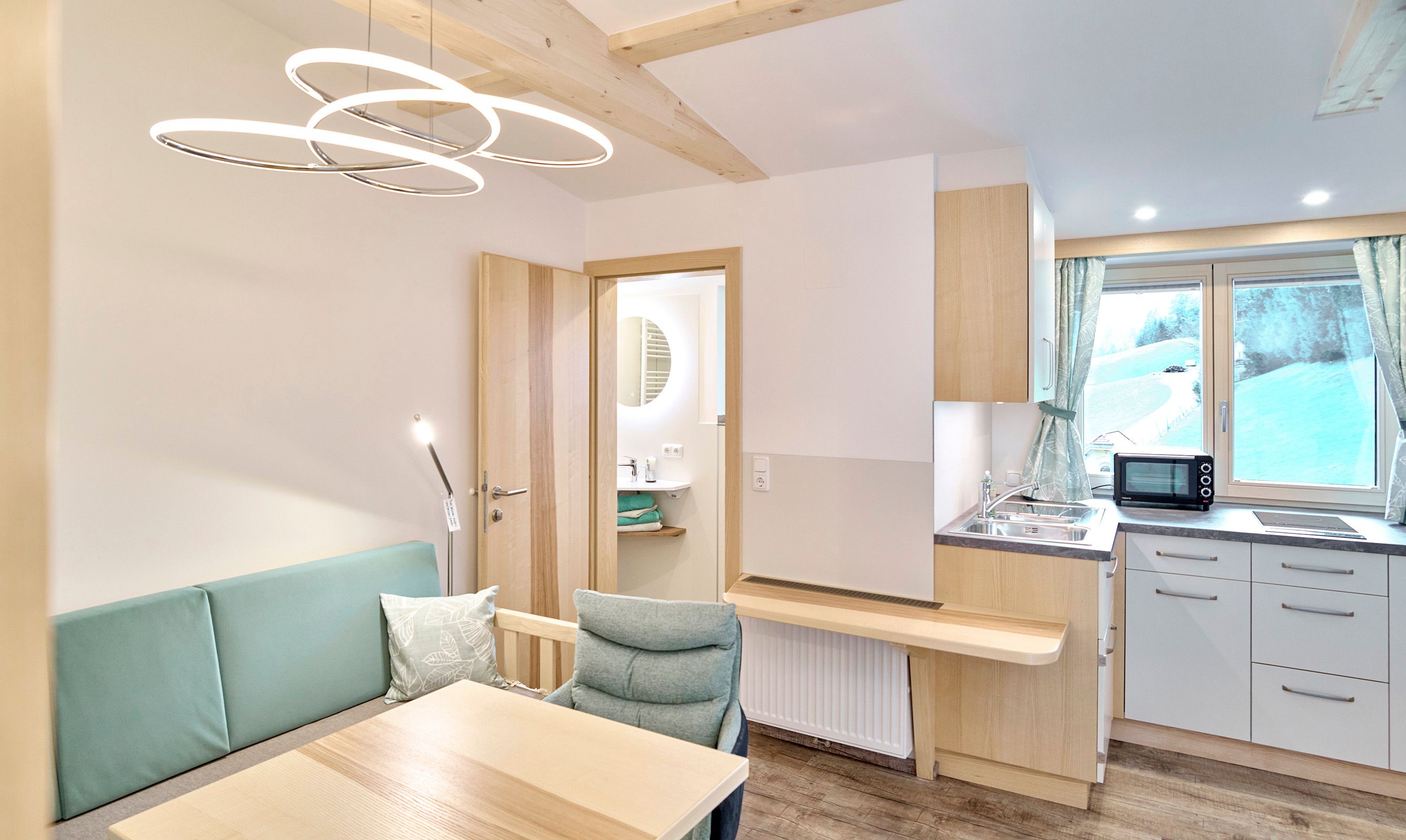 Modernes Apartment mit Holzmöbeln, kleiner Küche und Blick aus dem Fenster auf eine verschneite Landschaft.