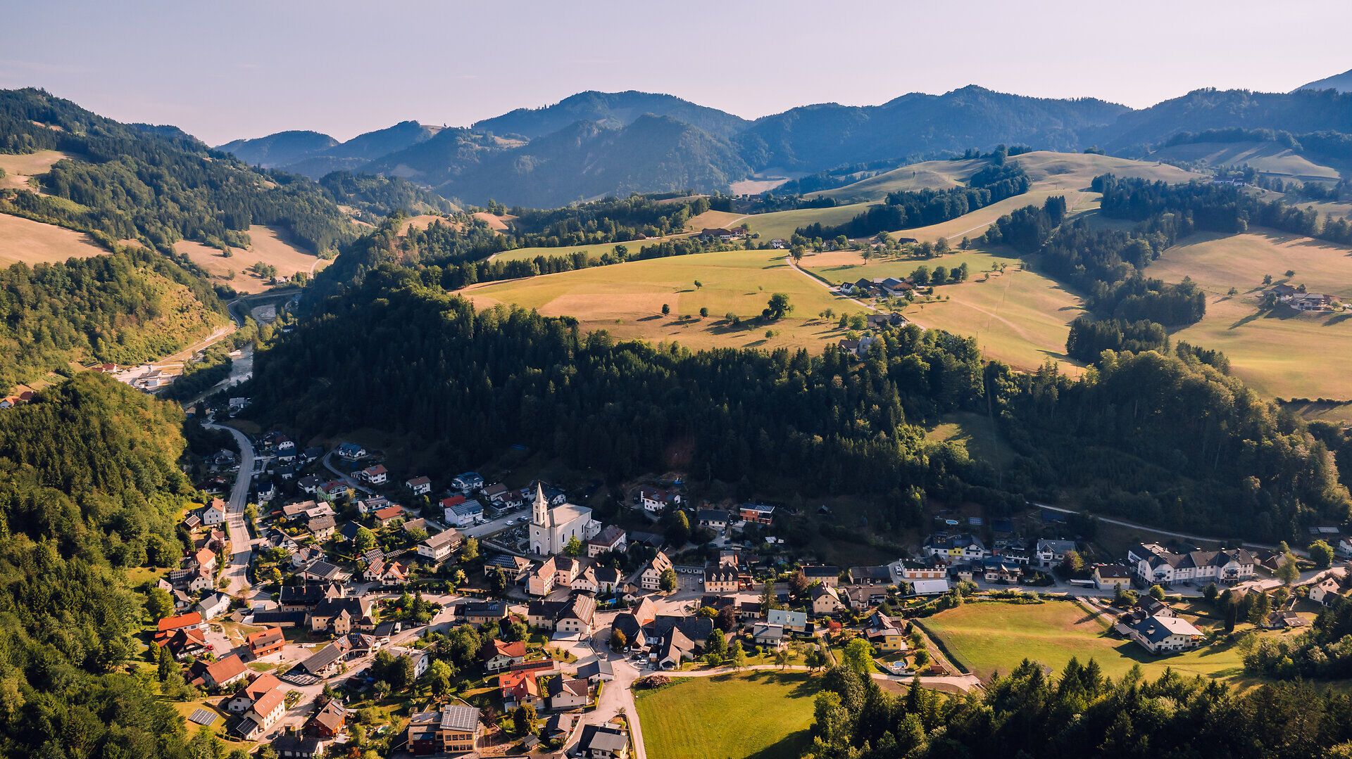 Luftaufnahme von Opponitz mit dem Ortszentrum, grünen Wiesen und bewaldeten Bergen im Hintergrund.