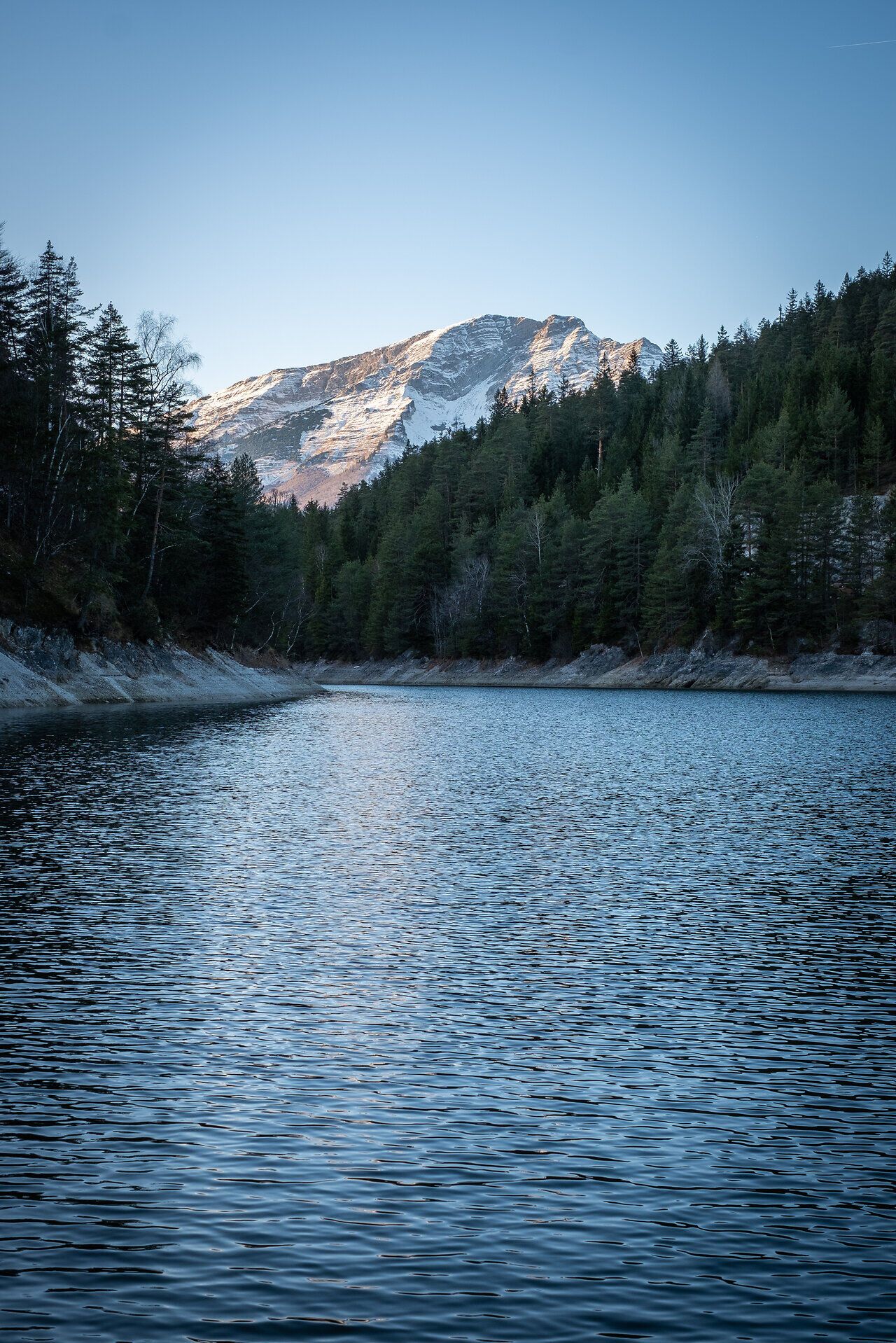 Die sanften Wellen des Erlaufstausees spiegeln die majestätischen Berge wider, während die winterliche Stille die Luft erfüllt. Umgeben von dichten Wäldern und schneebedeckten Gipfeln, lädt diese idyllische Landschaft zu einem unvergesslichen Naturerlebnis ein.