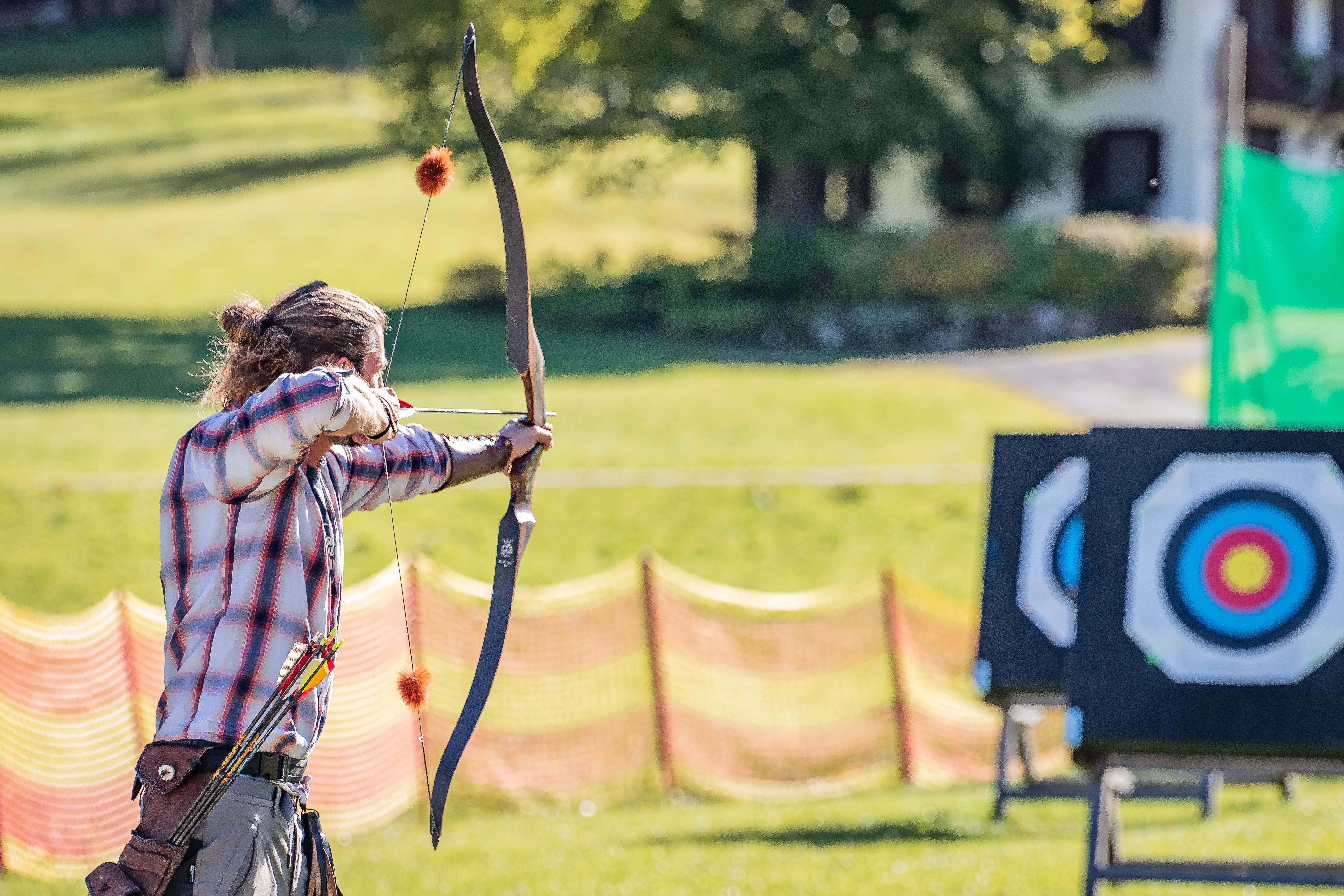 Mann hält Pfeil und Bogen und zielt auf eine Scheibe.