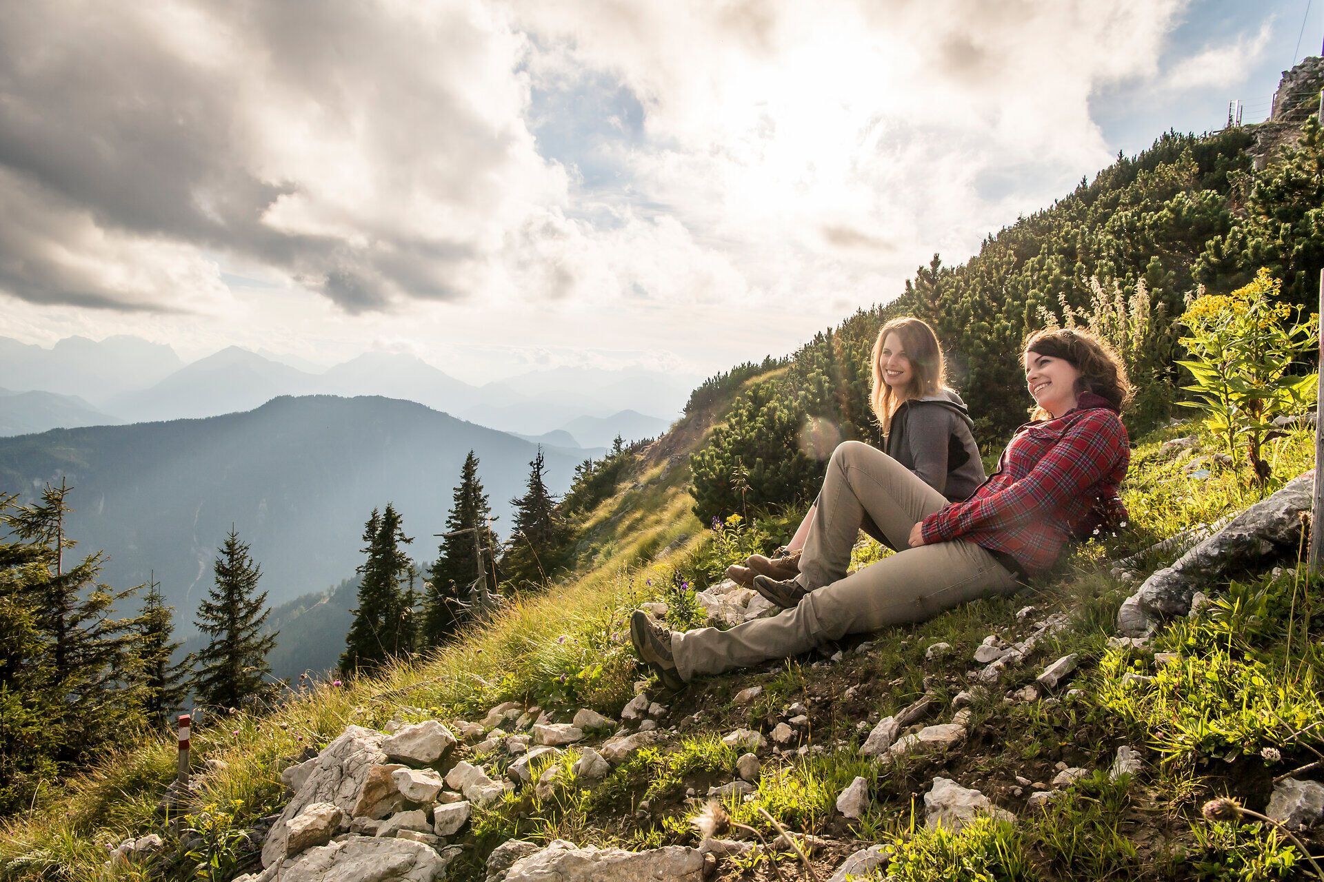 Inmitten der majestätischen Berge genießen zwei Wanderer die frische Bergluft und die atemberaubende Aussicht. Die sanften Hügel und die dichten Wälder schaffen eine perfekte Kulisse für unvergessliche Momente in der Natur.