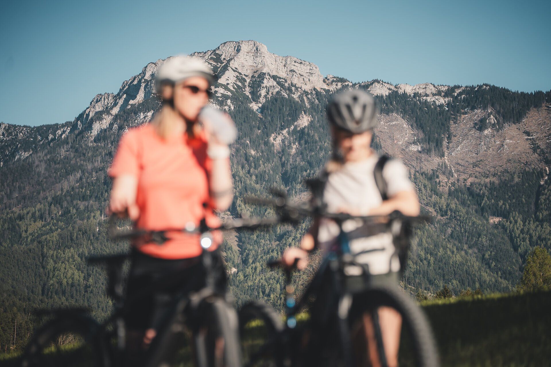Zwei Radfahrerinnen machen eine kurze Trinkpause, im Hintergrund die Berglandschaft.