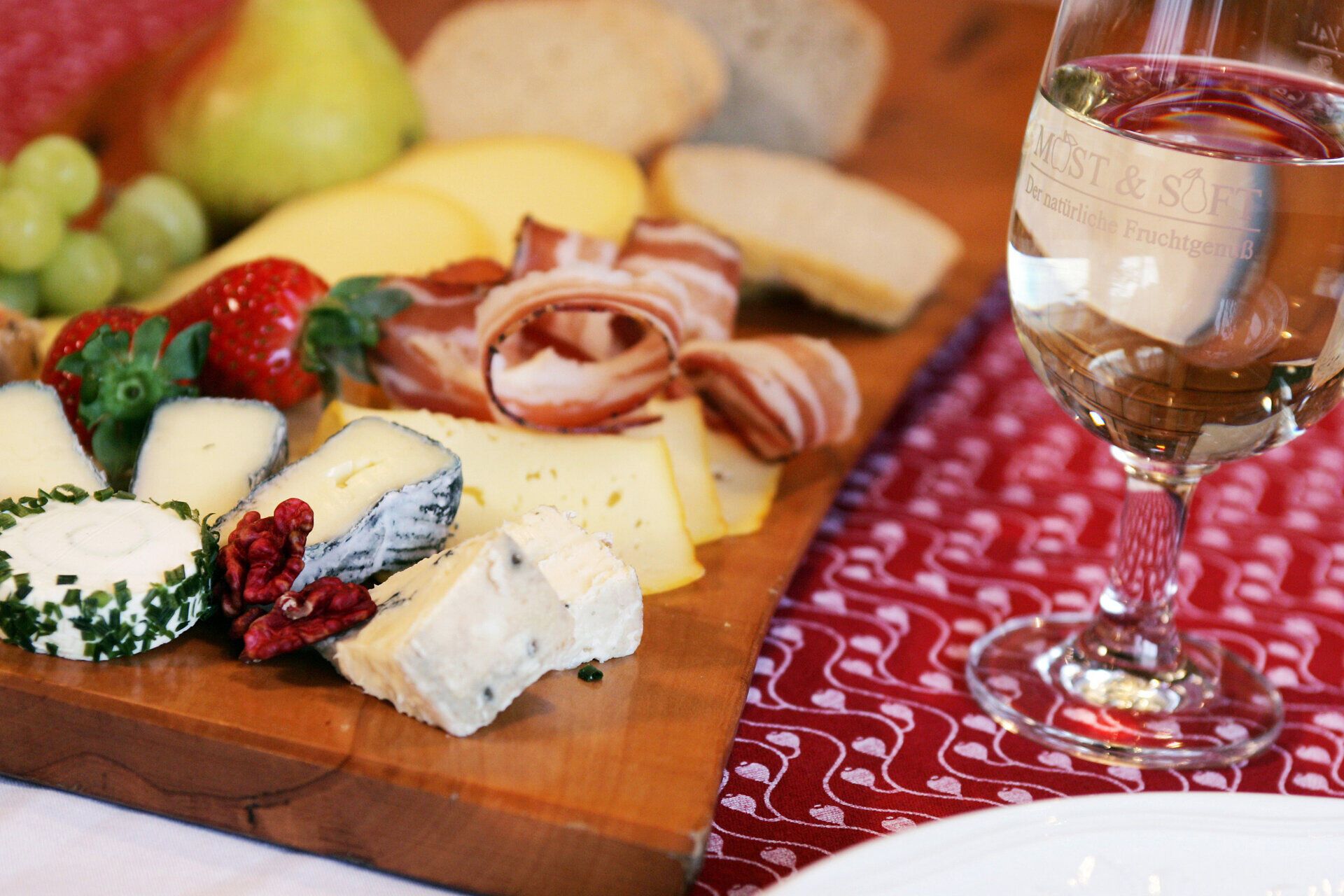Genießen Sie eine köstliche Jause mit einer Auswahl an feinen Käsesorten, frischem Obst und herzhaftem Schinken. Ein Glas erfrischender Most rundet das Geschmackserlebnis ab und lädt zum Verweilen in geselliger Runde ein.