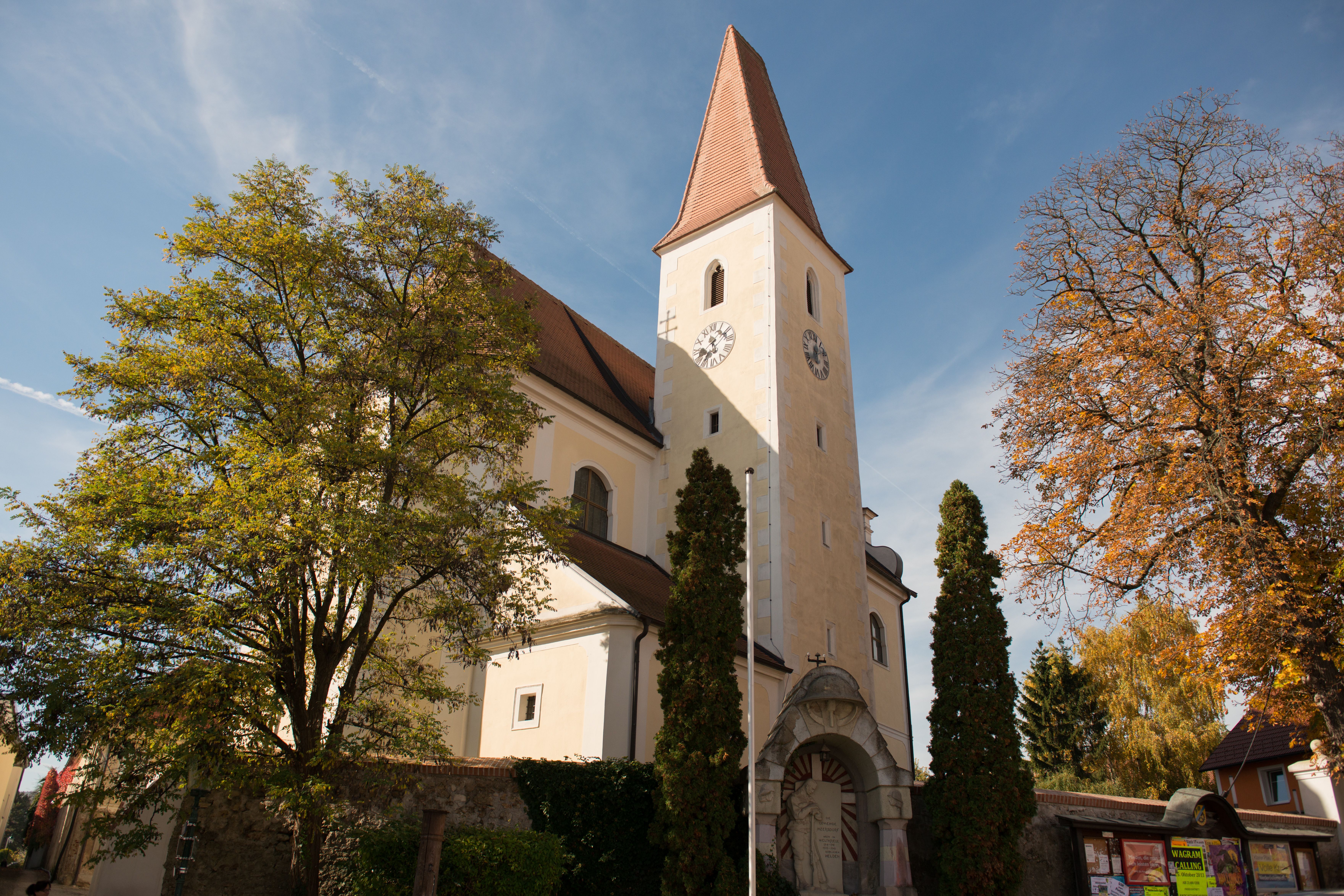 Kirche mit Turm und Uhr, umgeben von Bäumen im Herbst.