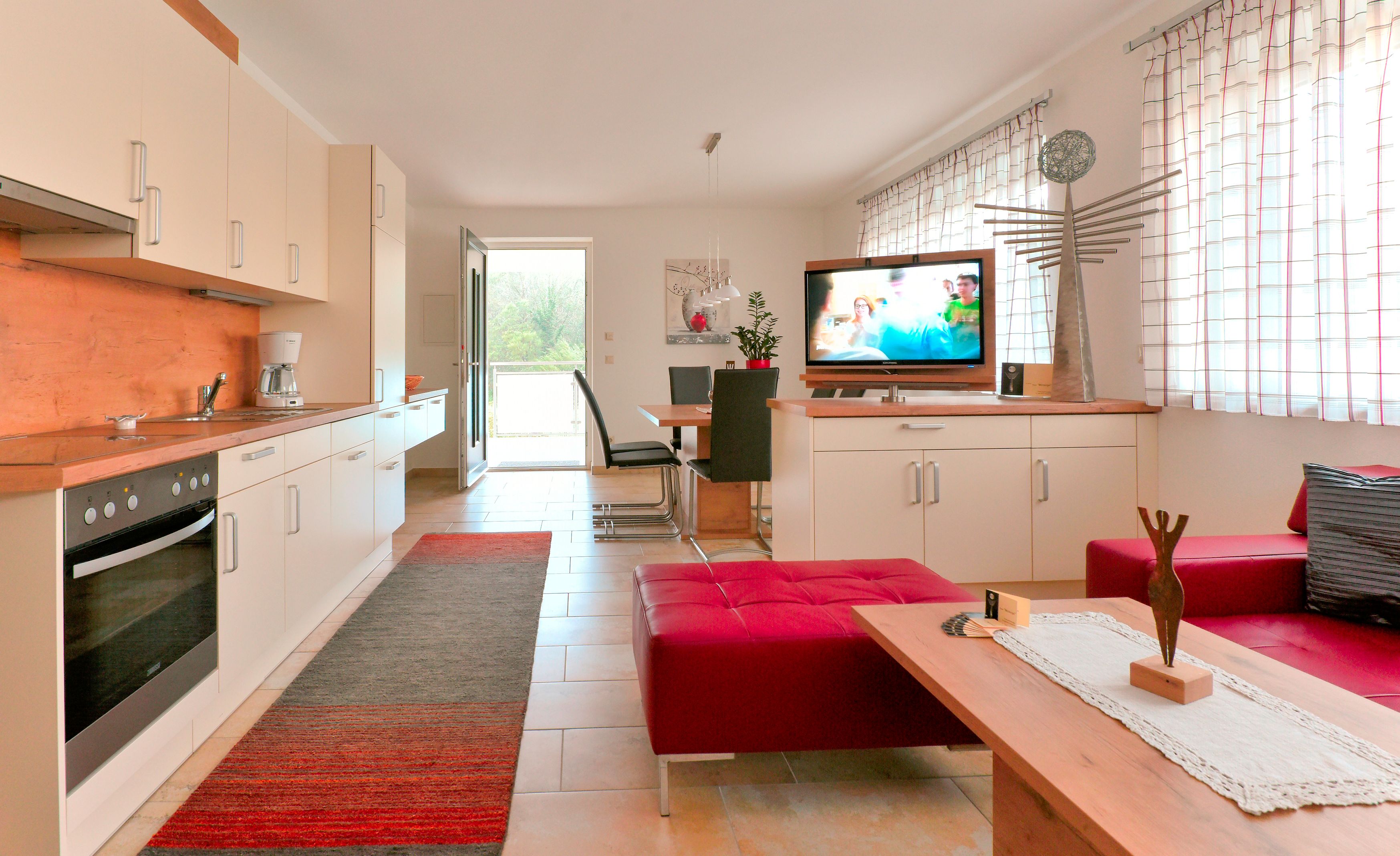 Moderne Wohnküche mit Einbauküche, Esstisch, Fernseher und roten Sitzmöbeln.