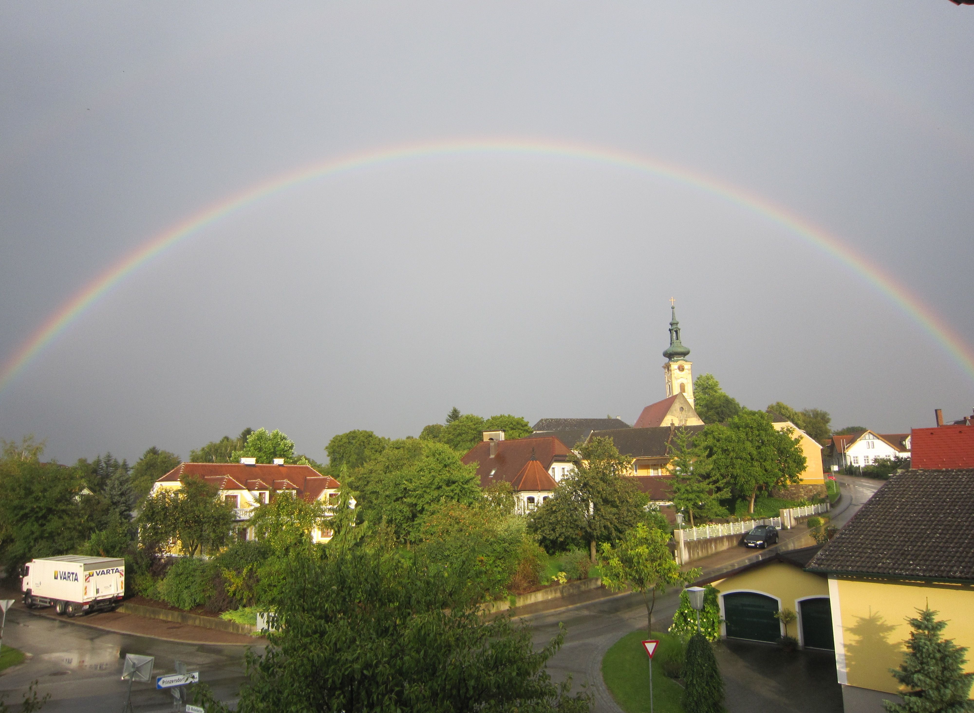 Ein Regenbogen spannt sich über ein Dorf mit Kirche und Häusern in Gerersdorf.