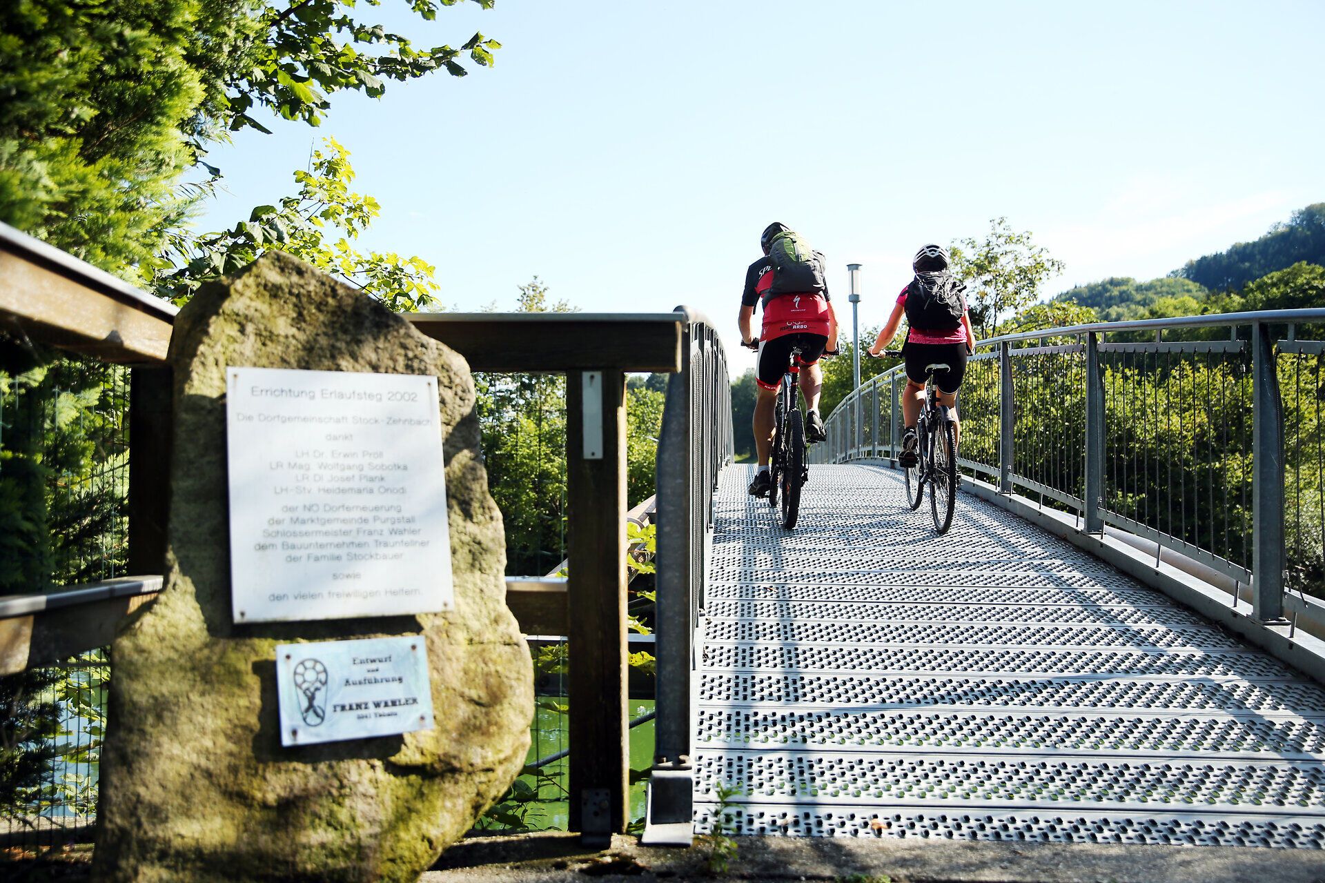 Ein Paar radelt entspannt über eine moderne Brücke, umgeben von üppigem Grün und der sanften Hügellandschaft des Erlauftals. Die frische Luft und die malerische Aussicht laden dazu ein, die Schönheit der Natur in vollen Zügen zu genießen.