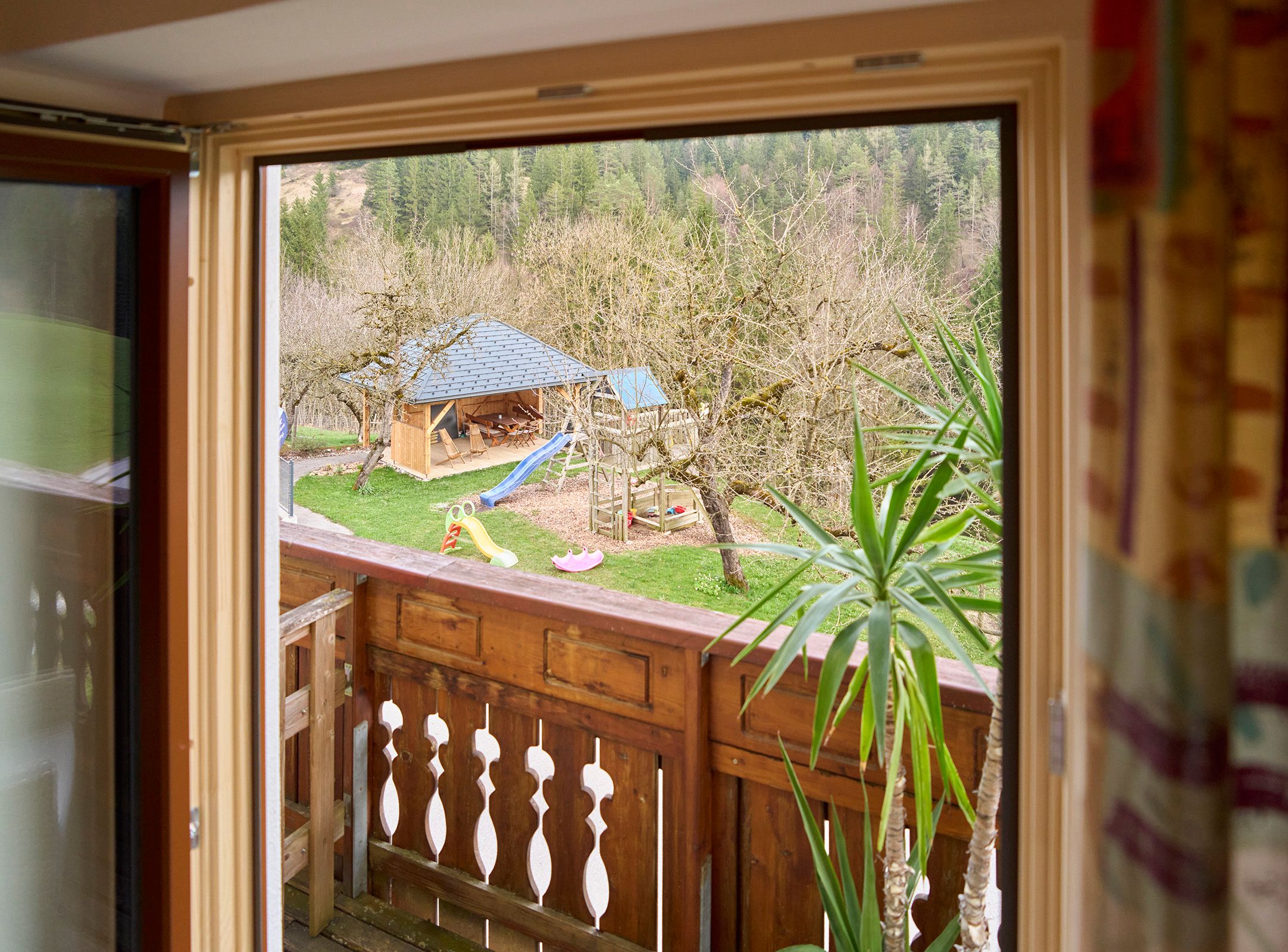 Blick aus einem Fenster auf einen Garten mit Spielplatz und Holzhütte.