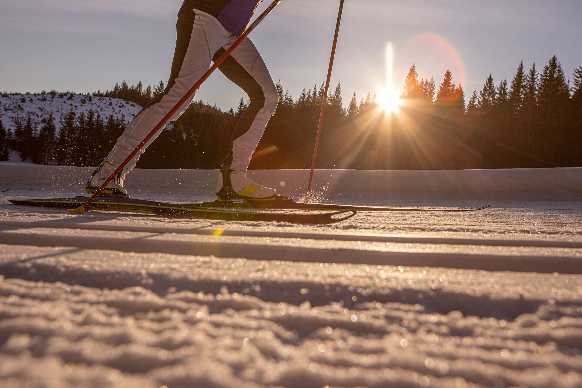 Die Sonne geht hinter den schneebedeckten Bergen auf und taucht die Landschaft in goldenes Licht. Langläufer gleiten elegant über die glitzernde, frische Schneedecke und genießen die ruhige, klare Winterluft. Ein unvergessliches Erlebnis für alle Wintersportbegeisterten in dieser malerischen Umgebung.