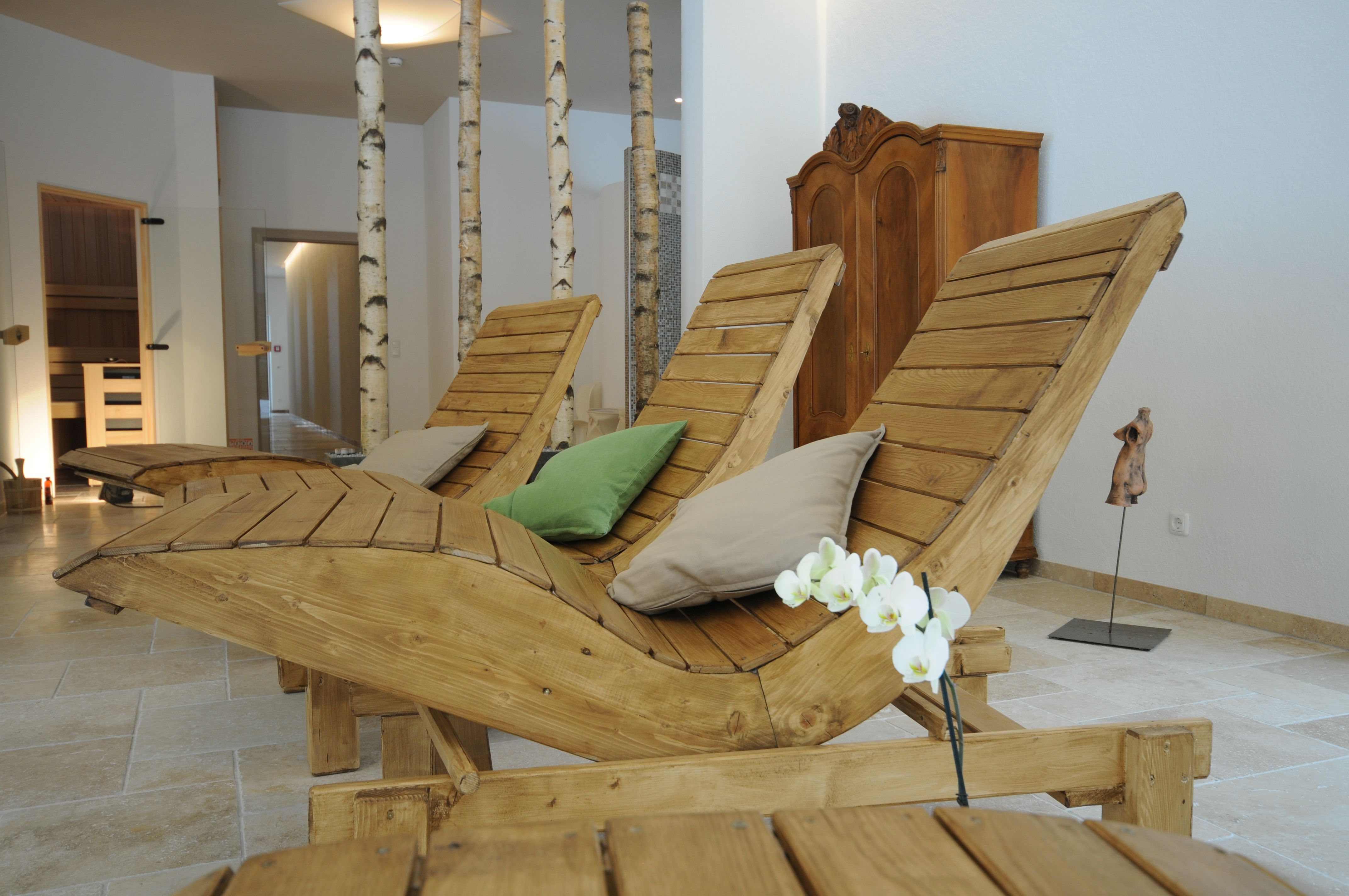 Innenansicht eines Wellnessbereichs mit Holzliegen, Kissen und Birkenstämmen.