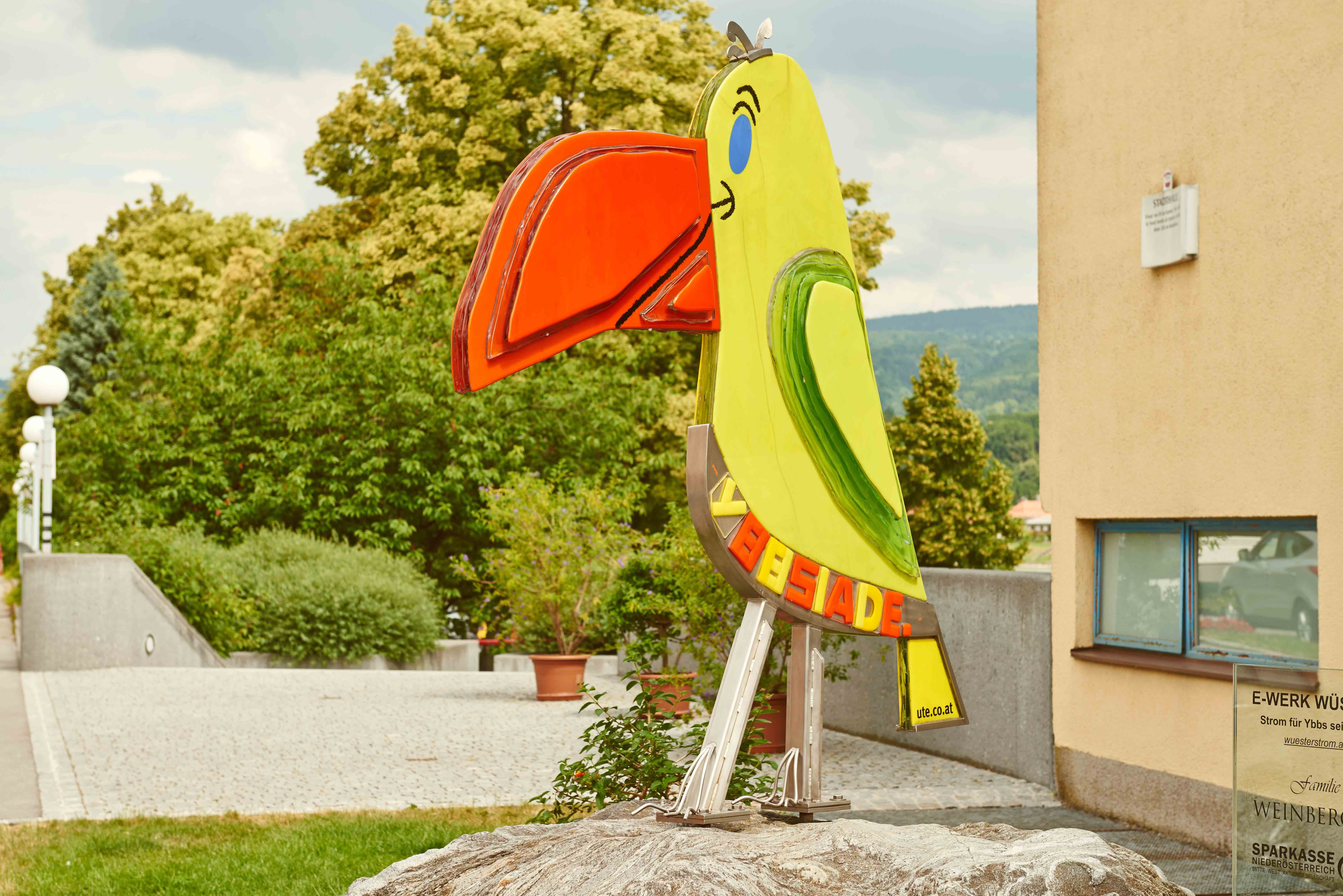 Bunte Papageienstatue in einer städtischen Umgebung.