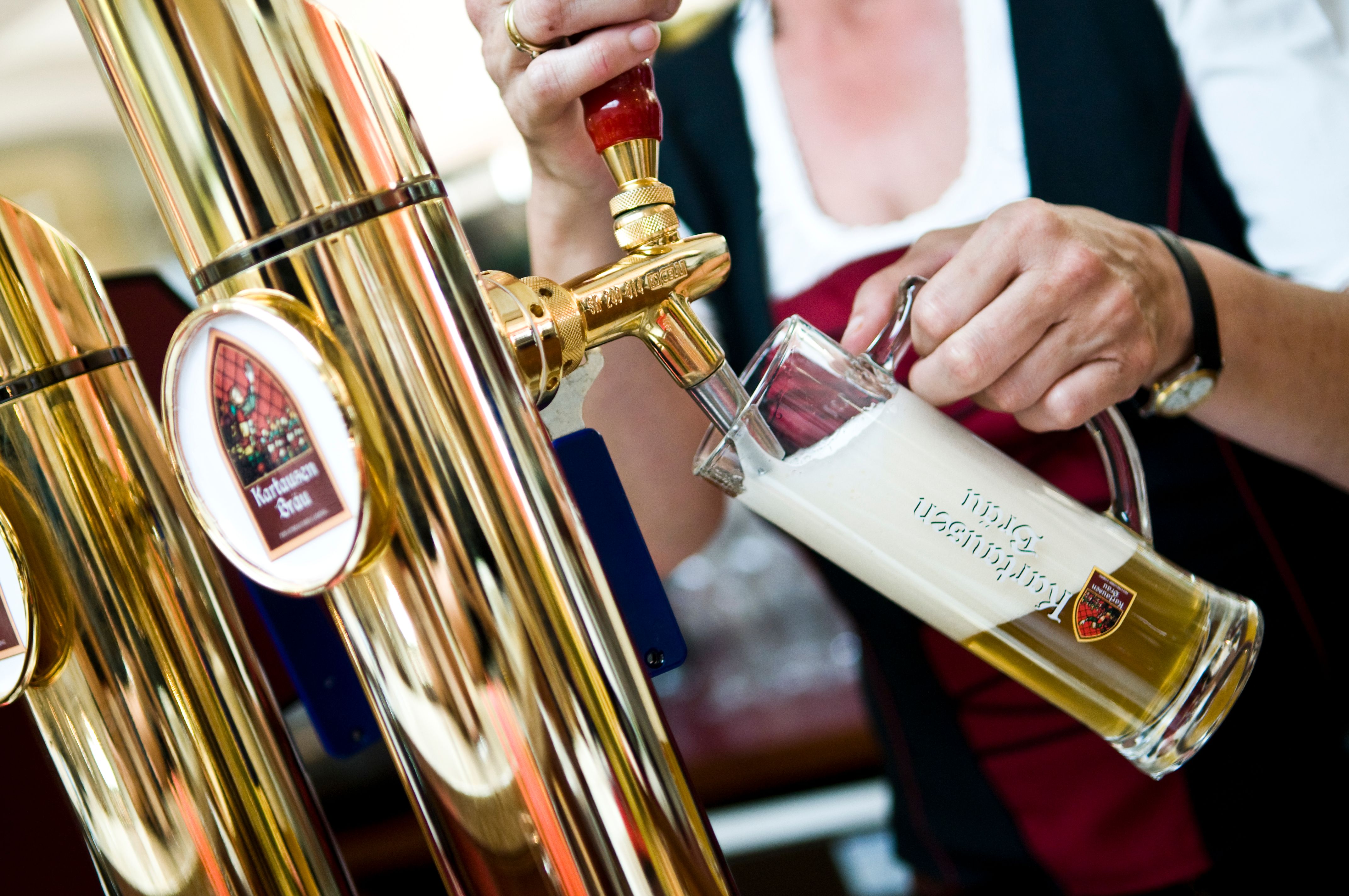 Eine Person zapft Bier aus einem goldenen Zapfhahn in ein Glas mit Schaumkrone.