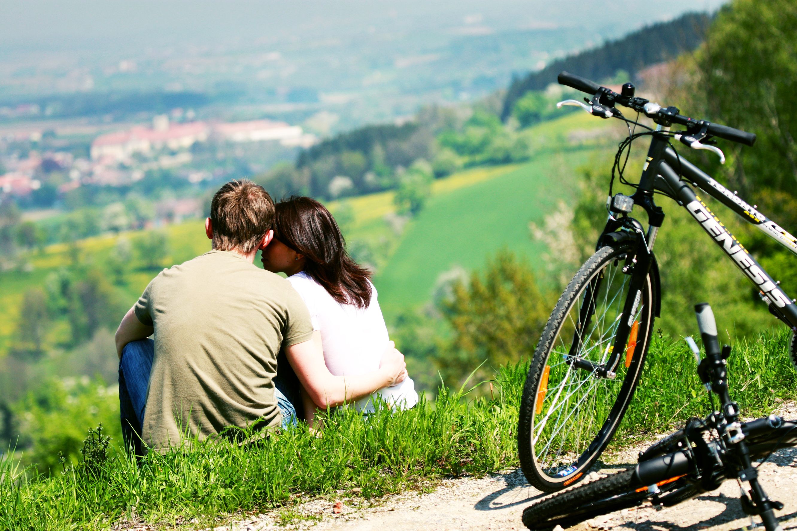 Ein Paar sitzt auf einer Wiese mit Blick auf eine Landschaft, daneben stehen Fahrräder.