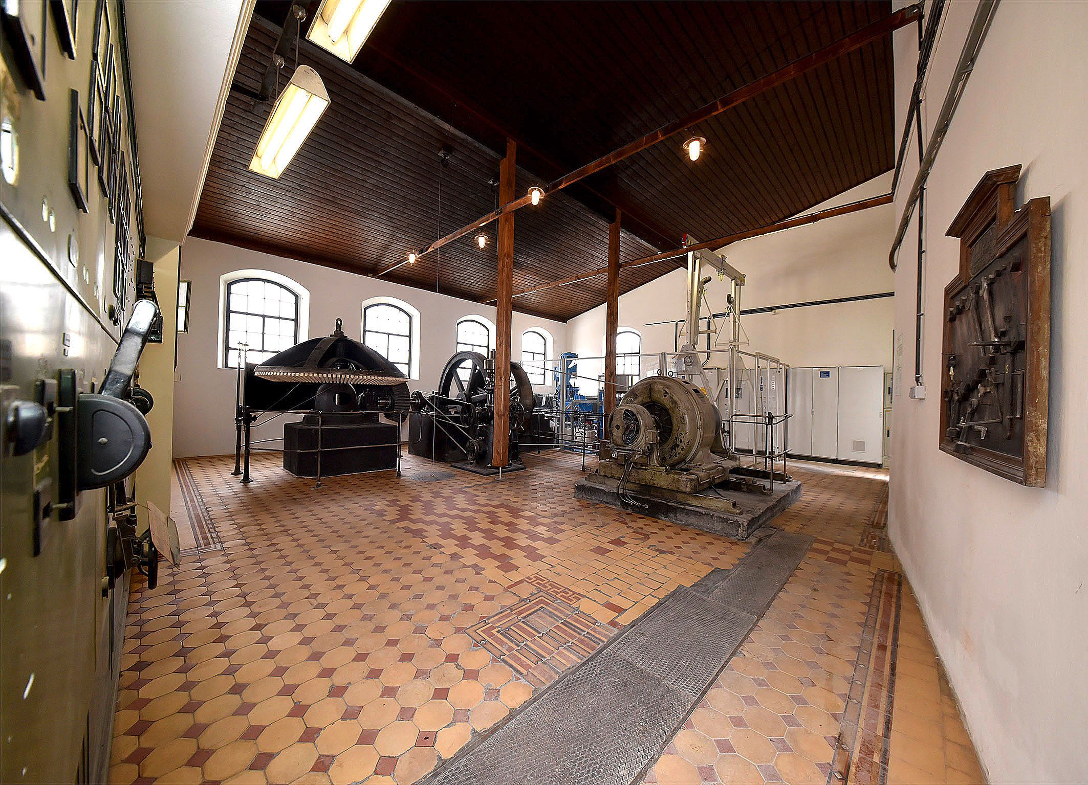 Innenansicht eines historischen Kraftwerks mit Maschinen und Geräten.