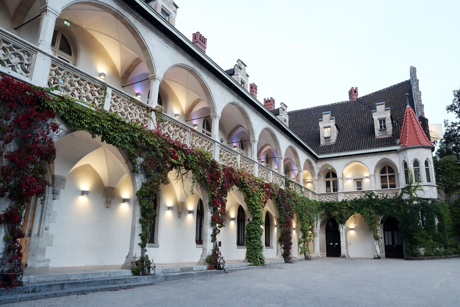 Umgeben von üppigem Grün und historischen Mauern strahlt das Schloss Rothschild eine einladende Atmosphäre aus. Die sanften Bögen und die blühenden Pflanzen verleihen dem Ort einen Hauch von Romantik und laden dazu ein, die Schönheit der Natur zu genießen.