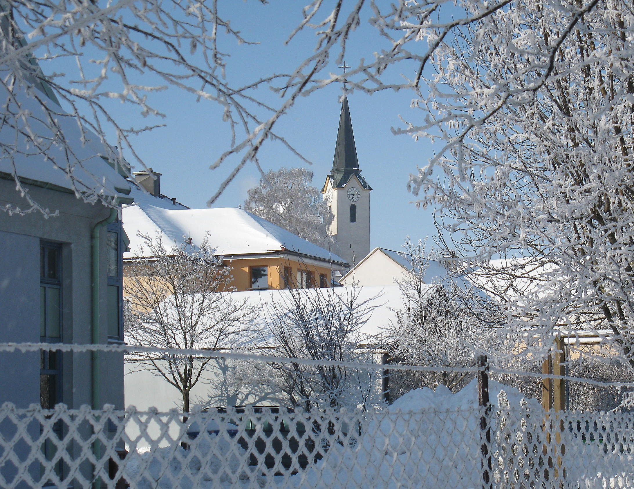 Verschneite Dorfansicht mit Kirche und Bäumen im Winter.