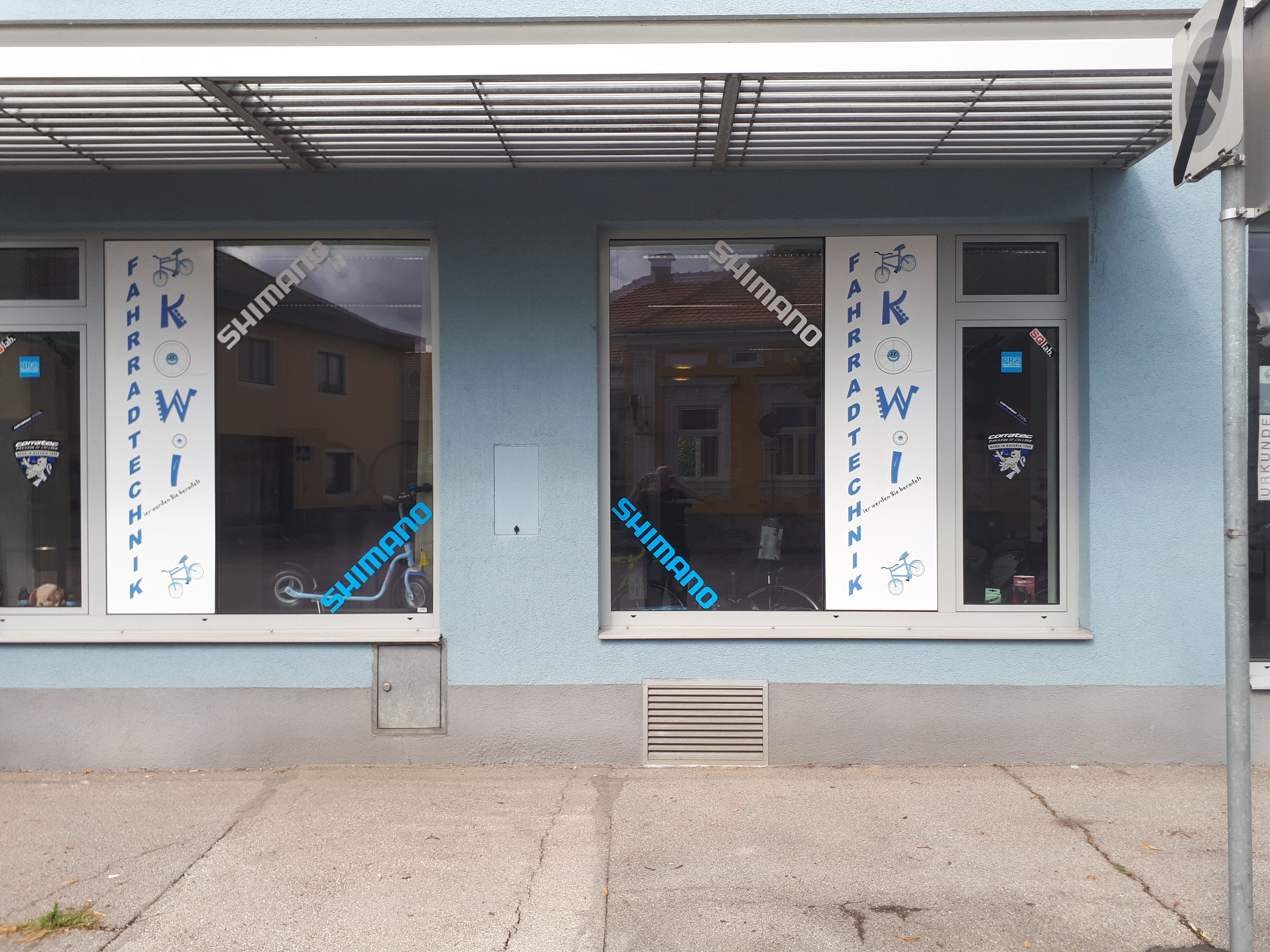 Fahrradgeschäft mit blauer Fassade und Schaufenstern mit Aufschrift 'Fahrradtechnik KOWI'.