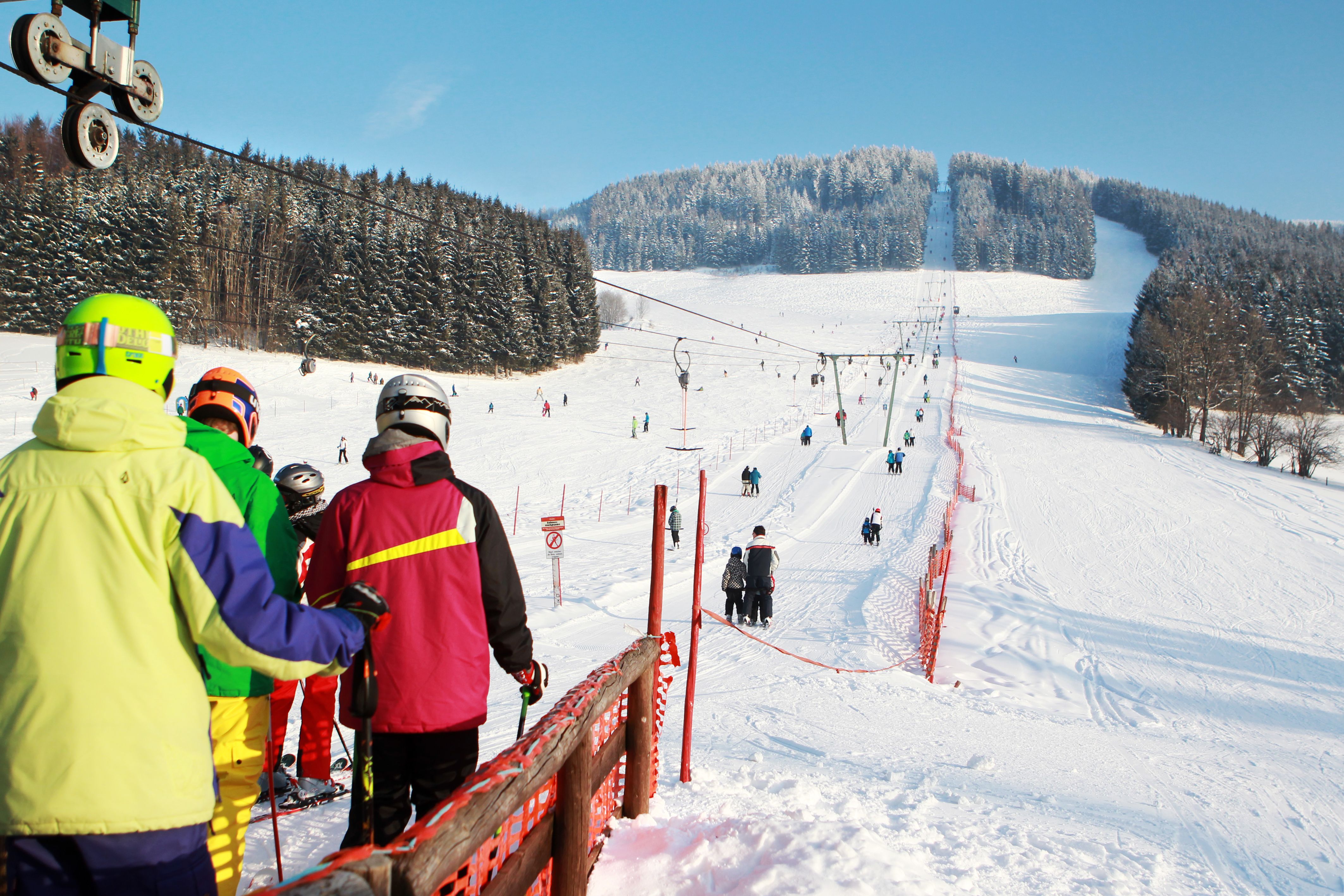Skifahrer stehen in einer Schlange am Skilift auf einer verschneiten Piste.
