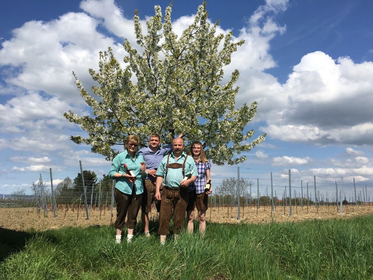 Vier Personen stehen vor einem blühenden Baum auf einem Feld.
