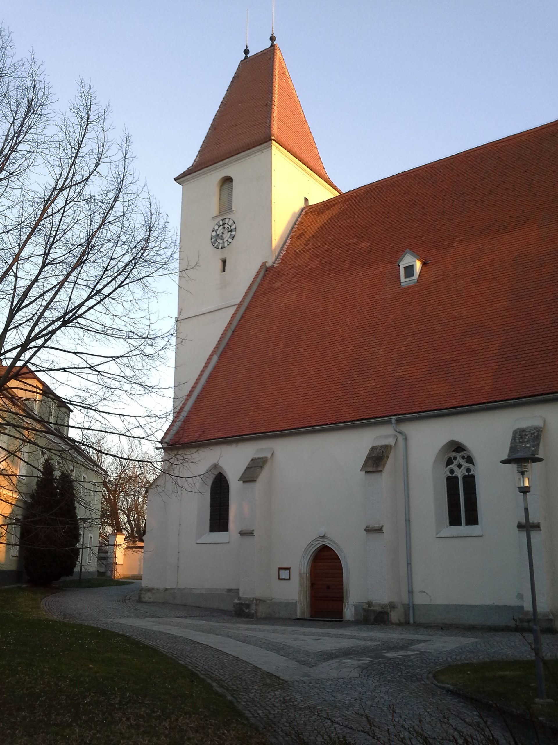 Kirche mit rotem Dach und Uhrturm in Kapelln bei Sonnenuntergang.
