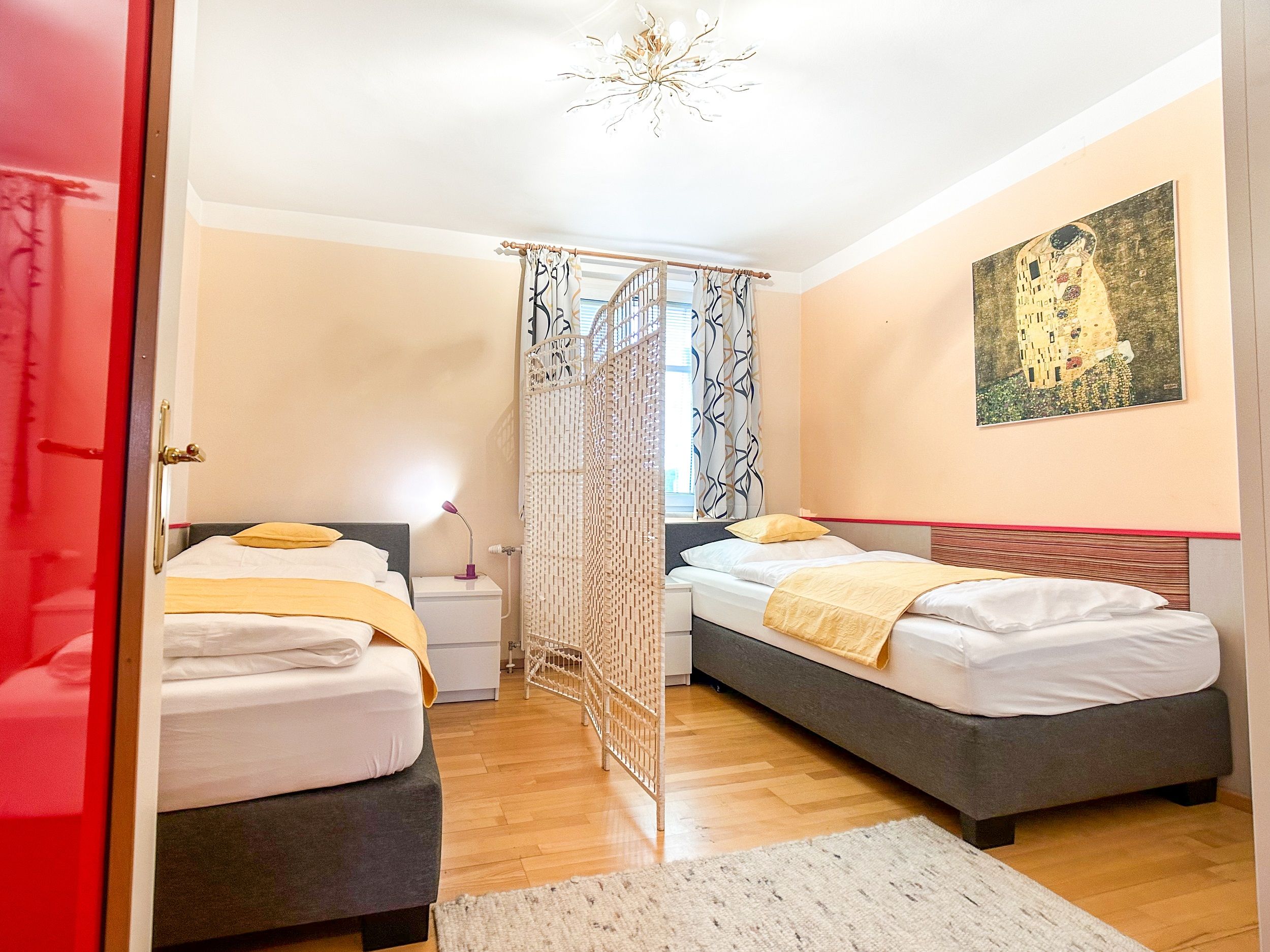 Schlafzimmer mit zwei Einzelbetten, gelber Bettwäsche, einem Raumteiler und einem Gemälde an der Wand.