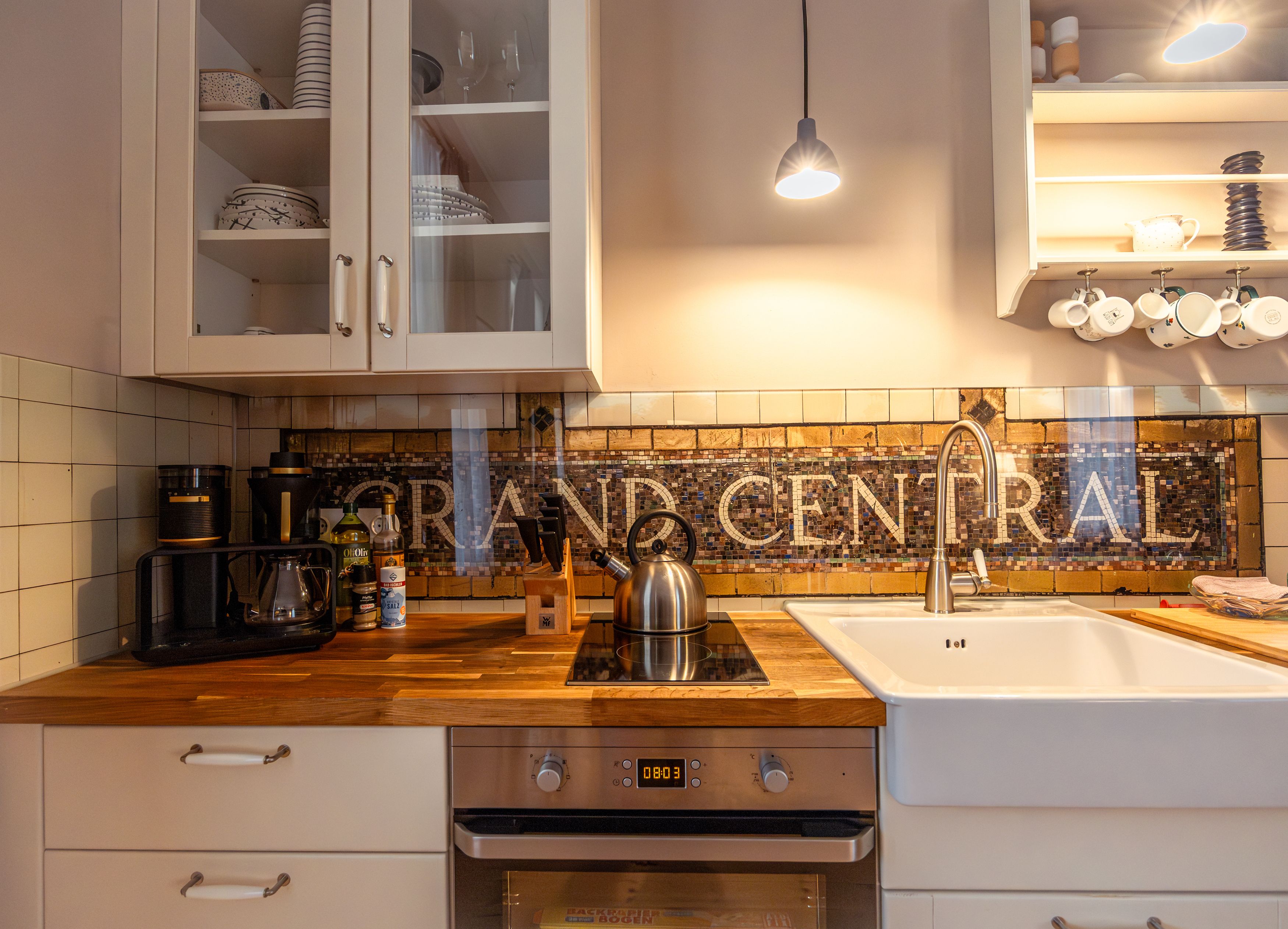 Küche mit Holztresen, Spüle, Herd und Mosaikfliesen mit 'GRAND CENTRAL'.