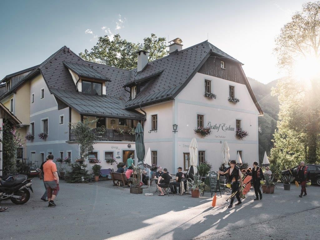 Ein traditionelles Gasthaus mit Menschen im Freien bei Sonnenschein.