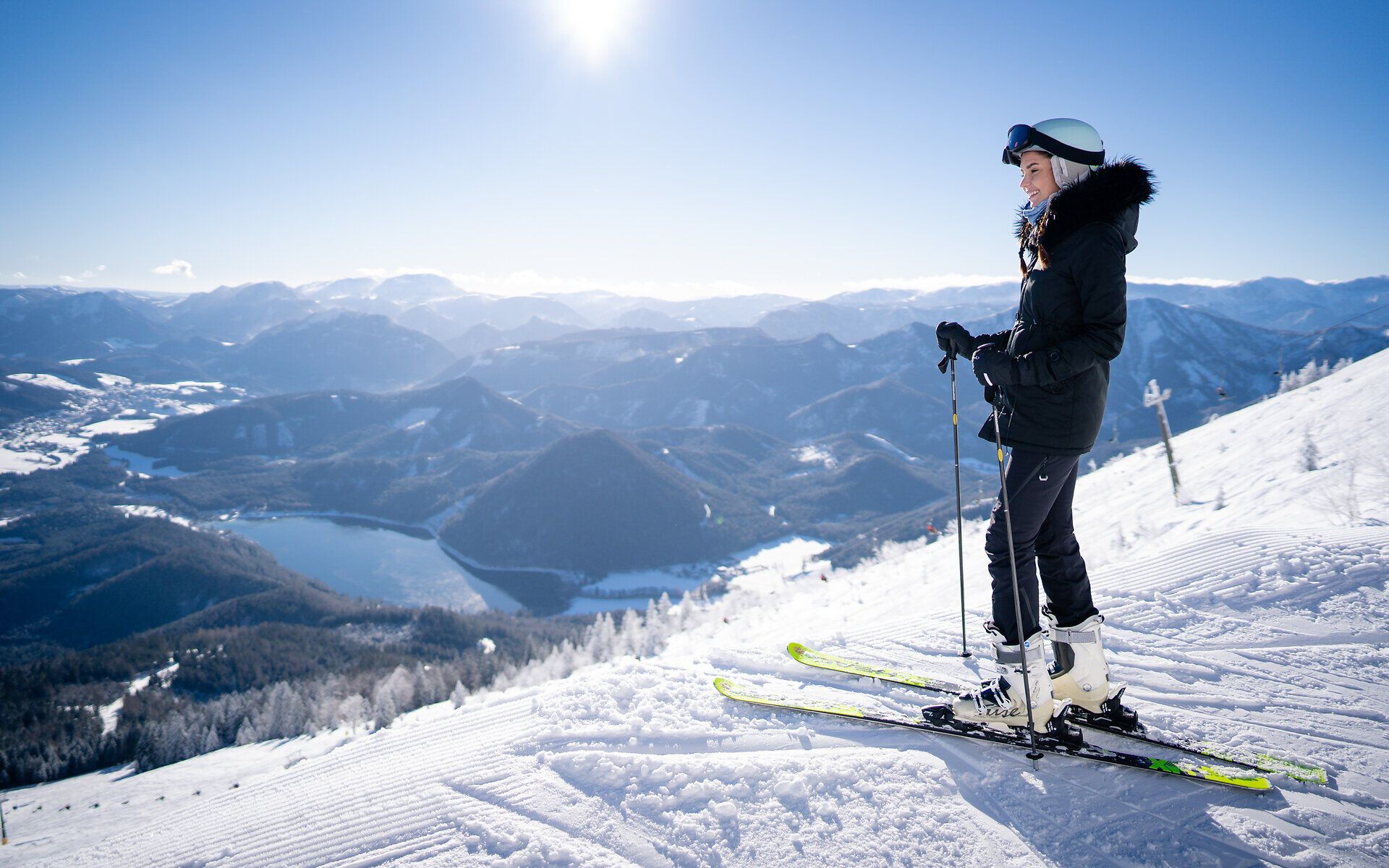 Die strahlende Wintersonne glitzert auf der schneebedeckten Landschaft, während eine Skifahrerin die frische Bergluft genießt. Umgeben von majestätischen Gipfeln und unberührtem Schnee, lädt dieser Ort zu unvergesslichen Abenteuern ein.
