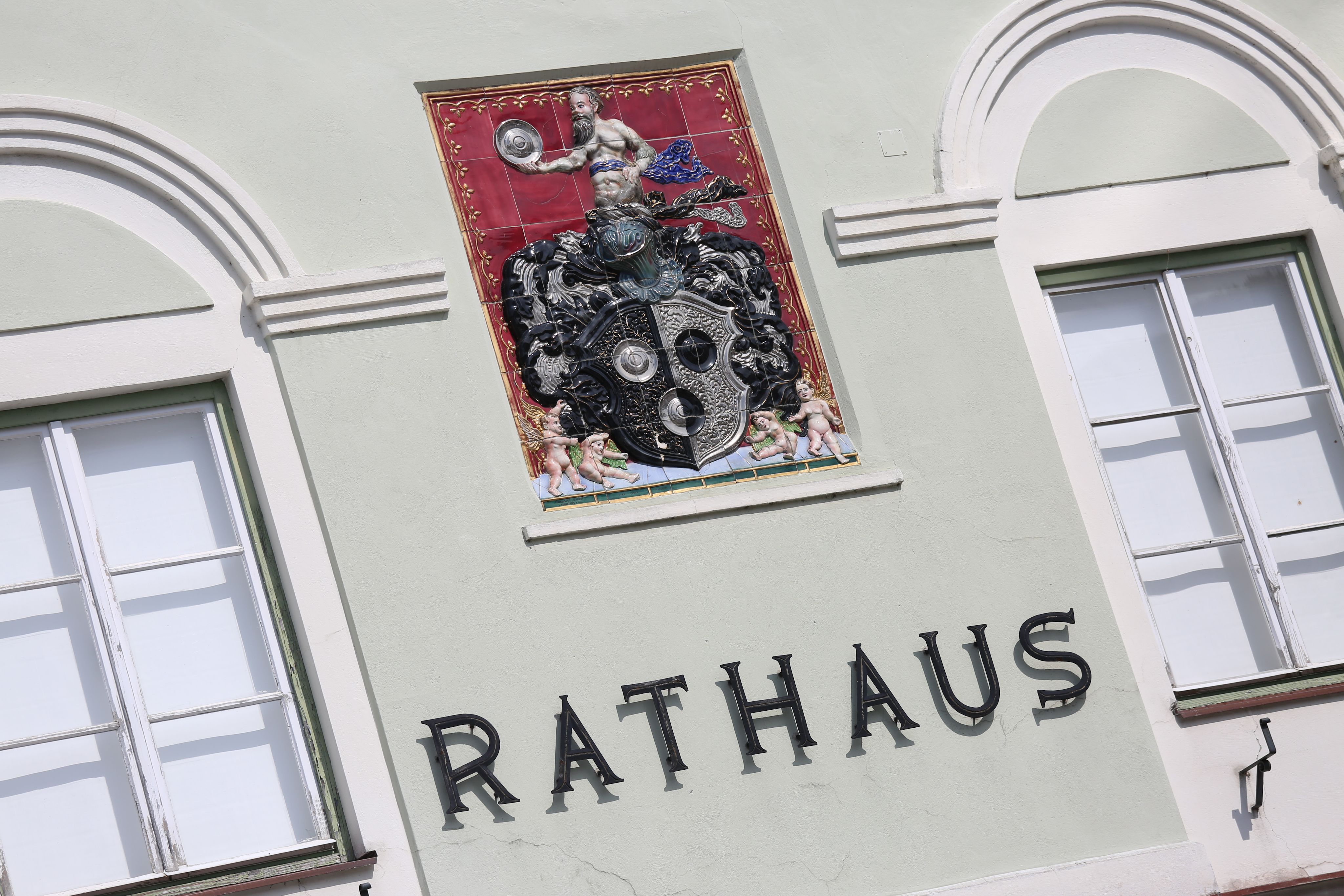 Fassade eines Rathauses mit dekorativem Wappen und Schriftzug 'Rathaus'.