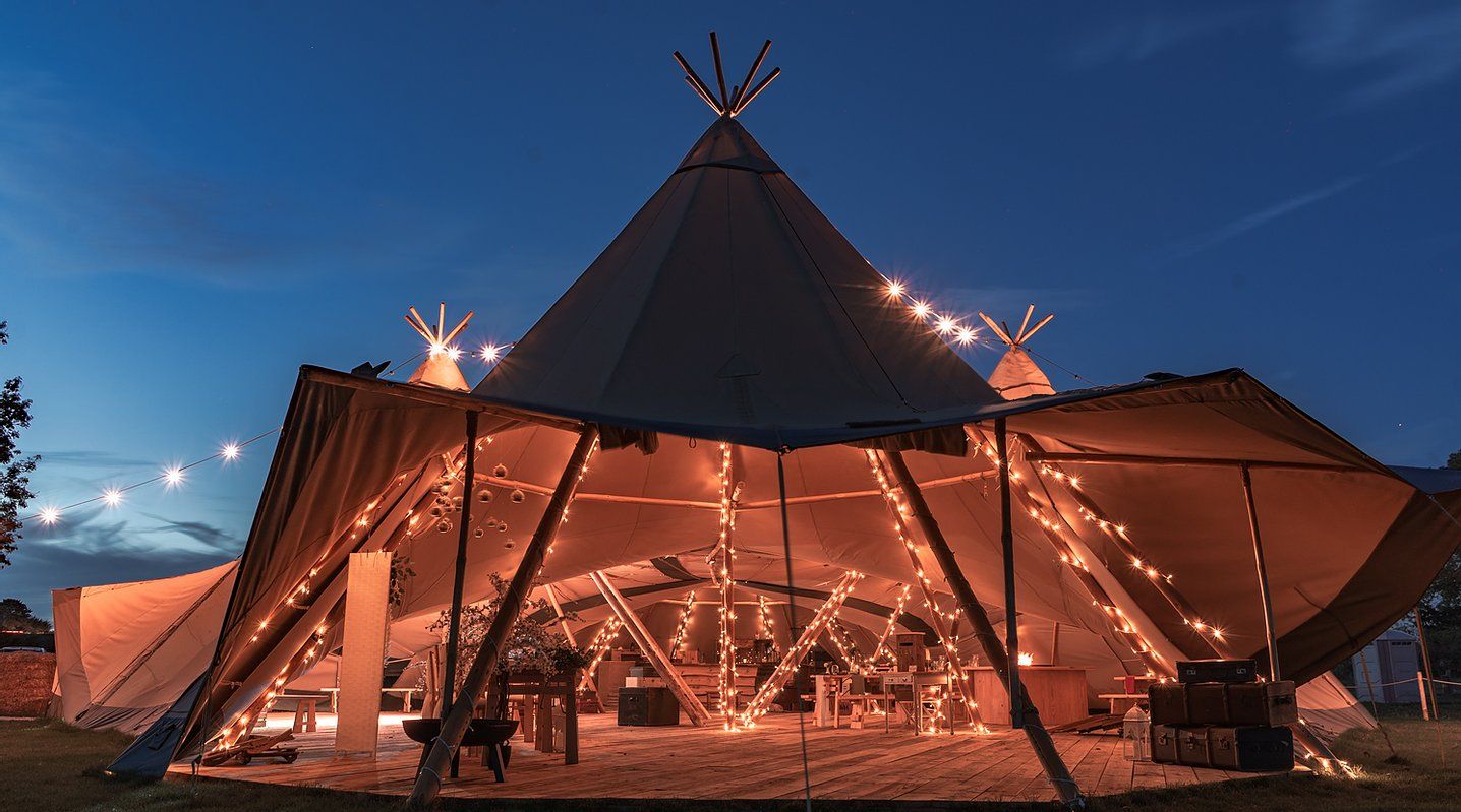 Ein beleuchtetes Tipi-Zelt bei Nacht, dekoriert mit Lichterketten, für eine Veranstaltung vorbereitet.
